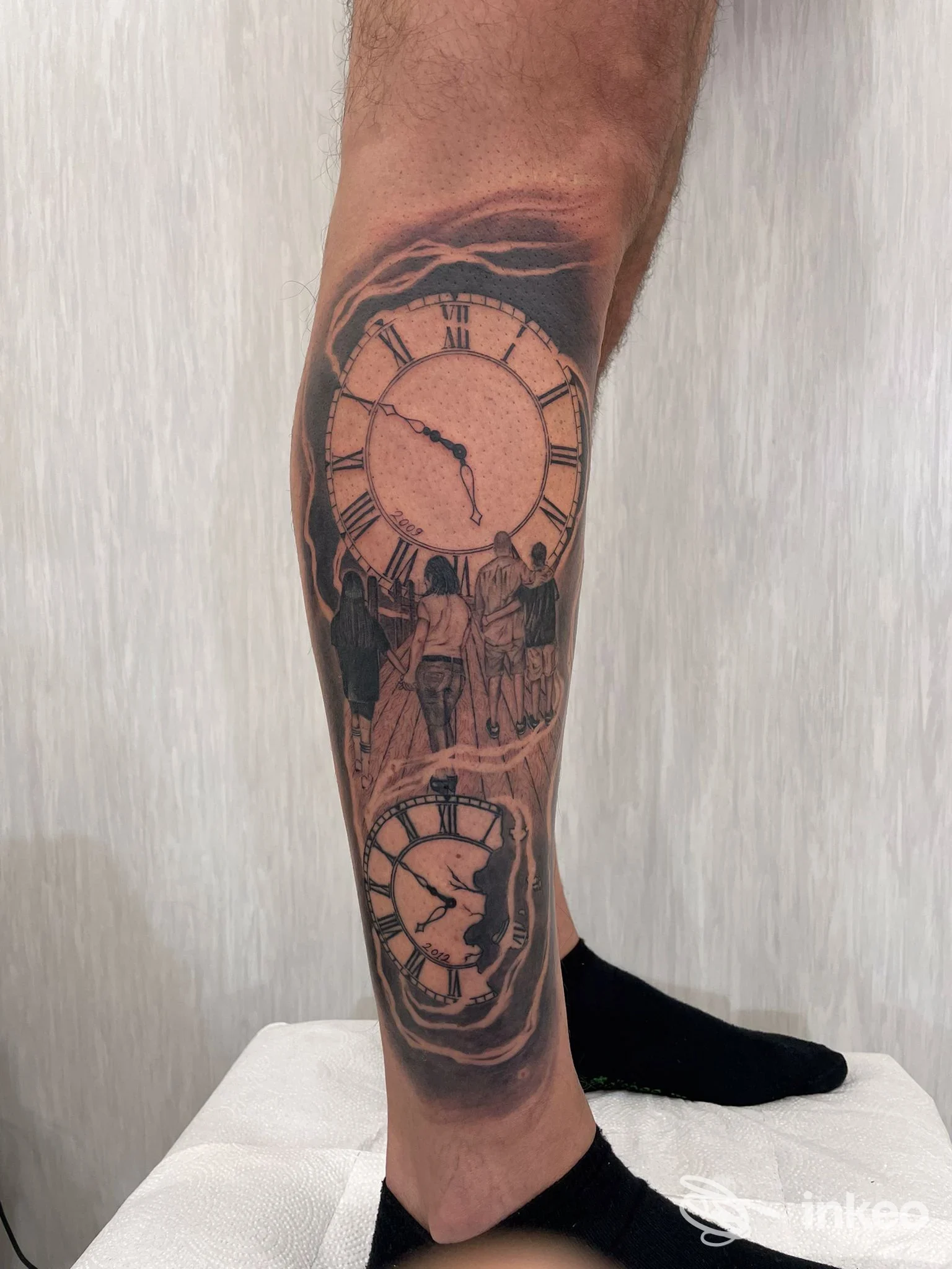 Tatuaggio sul polpaccio con due orologi e figure stilizzate in bianco e nero, fotografato su pelle reale. Eseguito da Supernatural Tattoo Studio, Volla.
