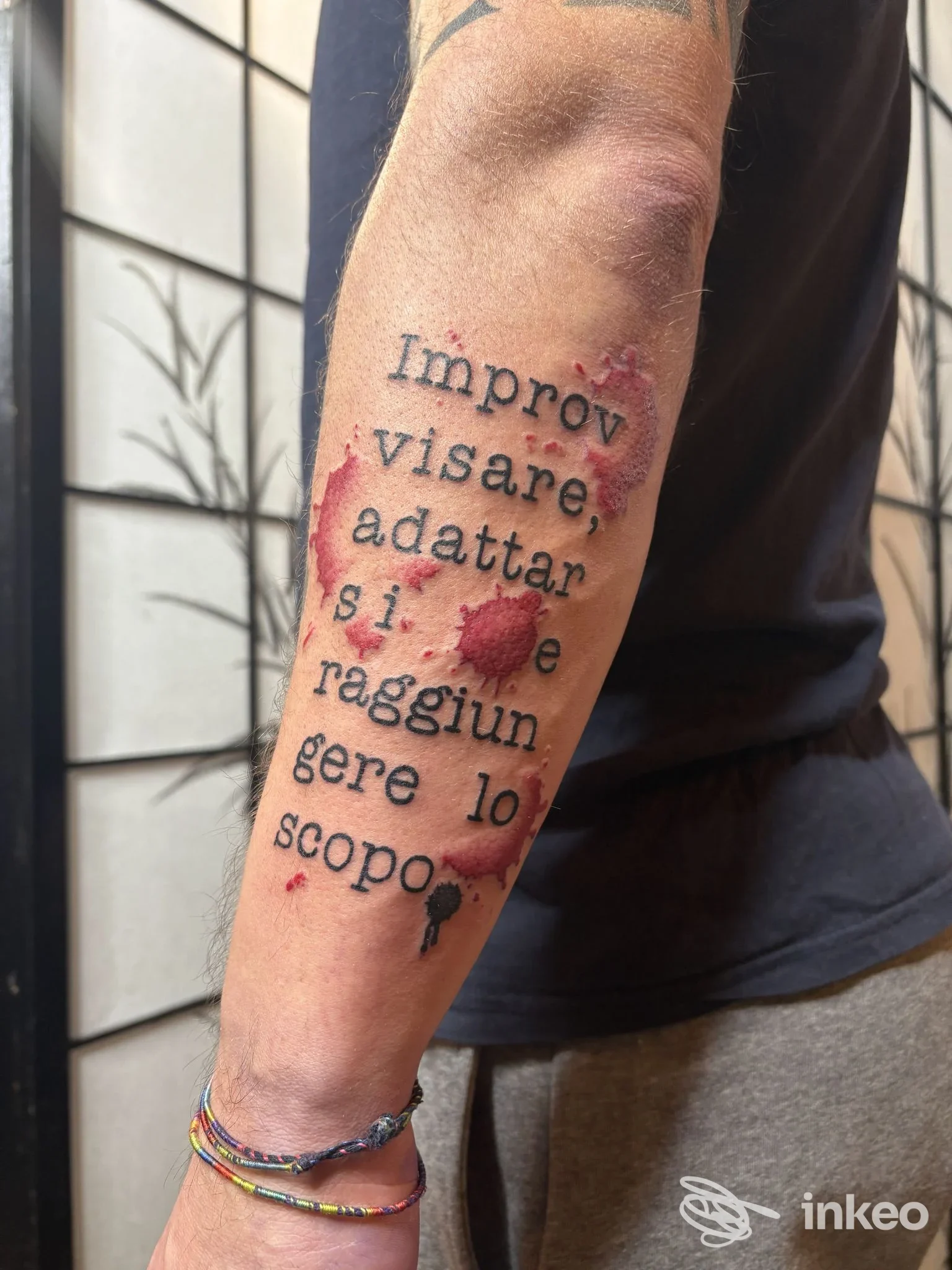 Tatuaggio testuale con schizzi rossi sull'avambraccio, foto per Pace e Inchiostro, Ferrara.
