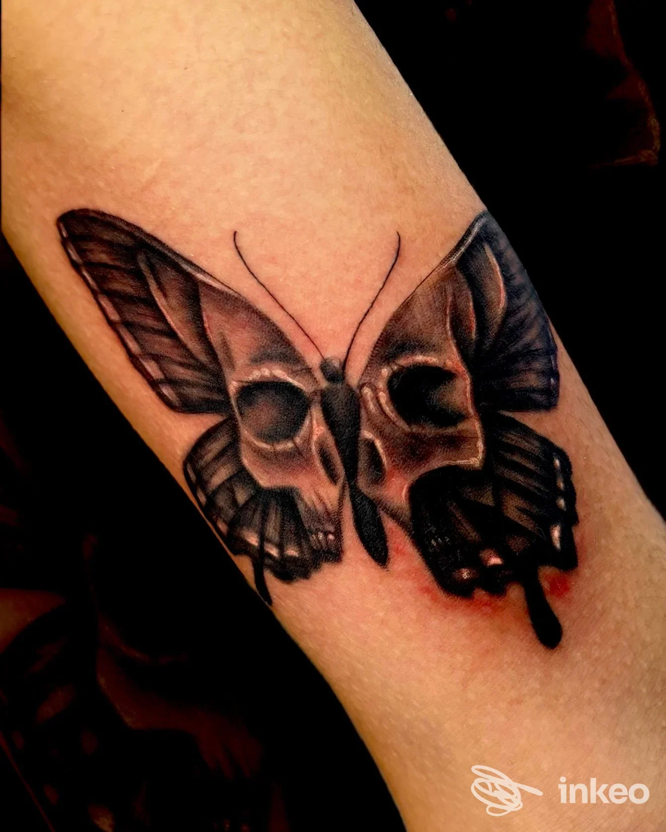 Tatuaggio su avambraccio: farfalla con elementi a forma di teschio in bianco e nero, realizzato da INK NIK Tattoo Studio a Cotignola.