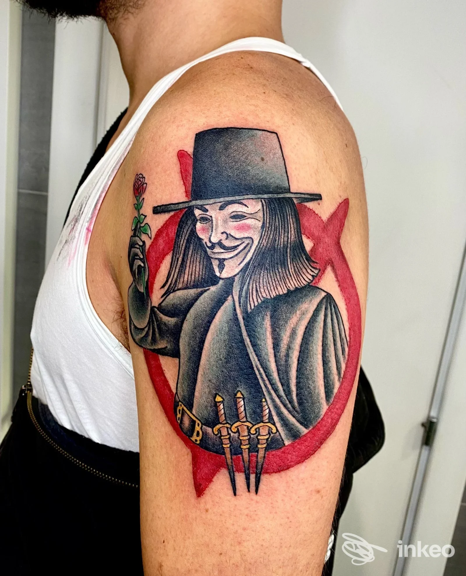Tatuaggio colorato sul deltoide con figura mascherata e fiore, eseguito da Magma Tattoo Club a Portici.