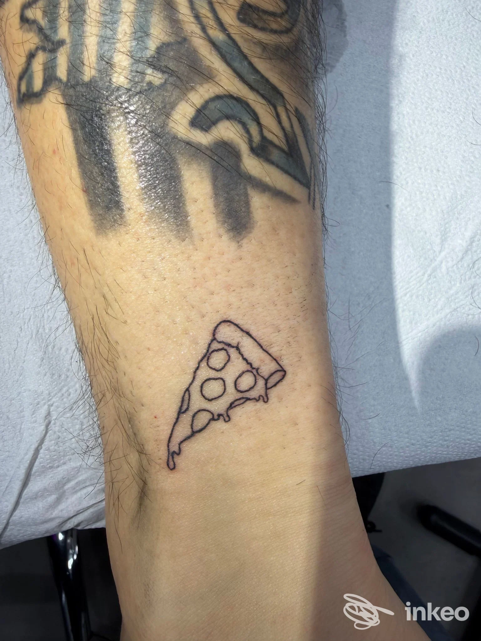 Piccolo tatuaggio a spicchio di pizza in outline sulla caviglia, foto scattata in studio Project Flash Tattoo a Napoli.