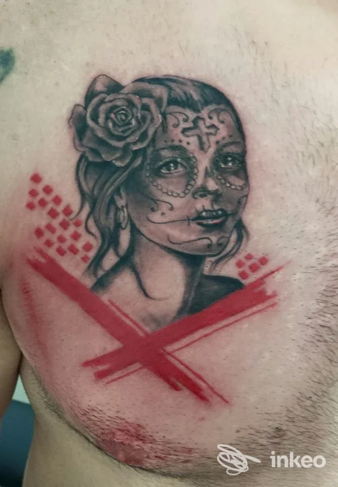 Tattoo sul torace raffigurante una donna con sugar skull e rosa nei capelli, con una pennellata rossa a croce attraversante sul petto.
