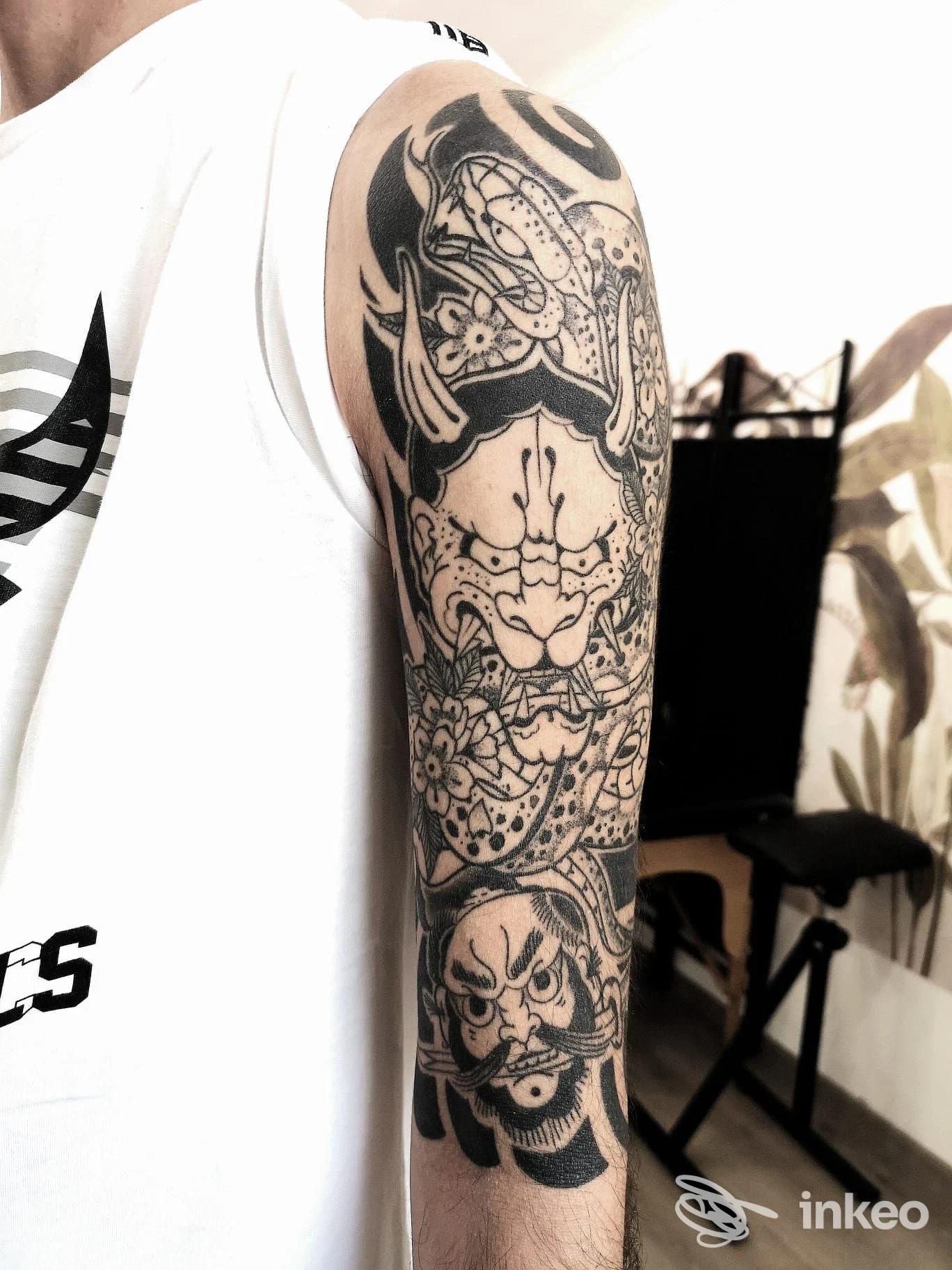 Manica tatuata ornamentale con maschere e fiori fotografata nello studio Alley Doll a Faenza, dettaglio sul braccio.