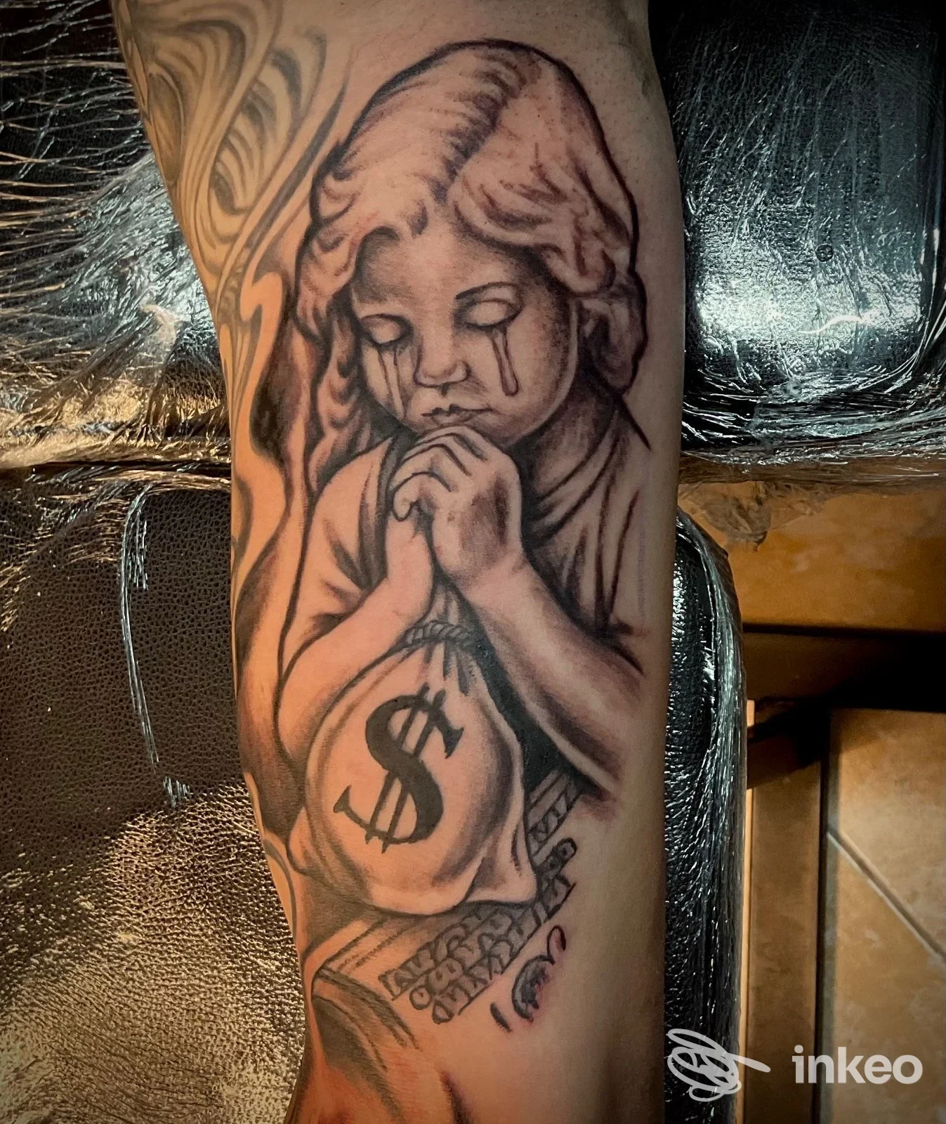 Tatuaggio black & grey su avambraccio: figura infantile che prega con una sacca con simbolo del dollaro. Seven Tattoo studio, Ostuni.