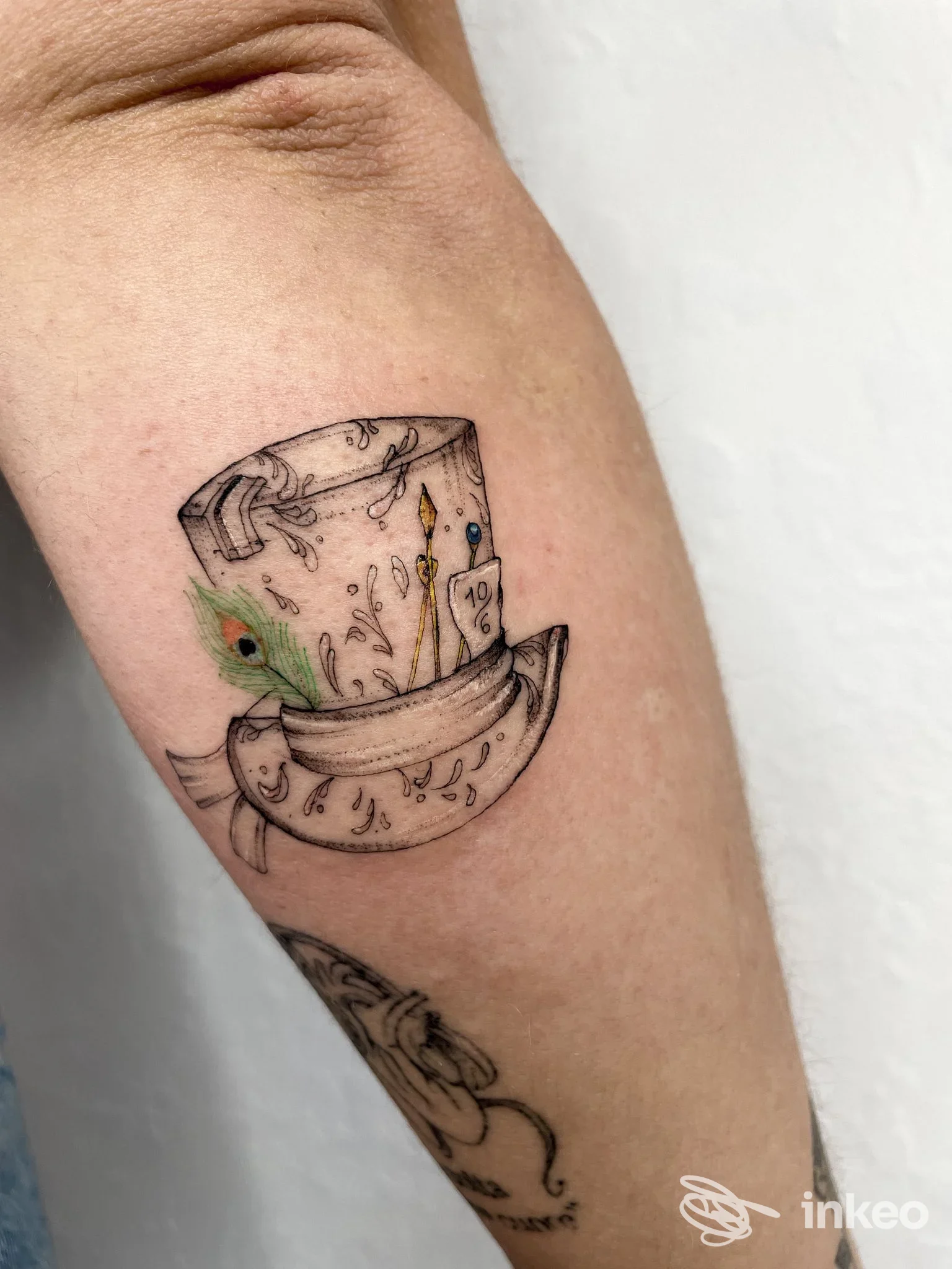 Tatuaggio su avambraccio interno raffigurante un cilindro con una piuma colorata, realizzato da Edera tattoo art a Perugia.