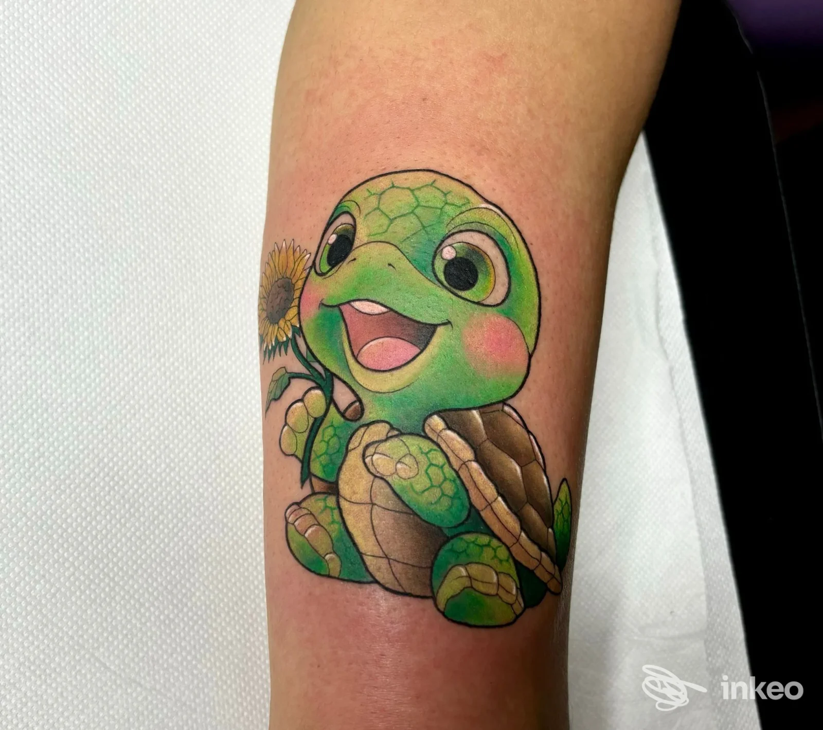 Tatuaggio colorato di una tartarughina stilizzata con girasole sull'avambraccio, realizzato da Electric Tattoo Studio ad Asti.