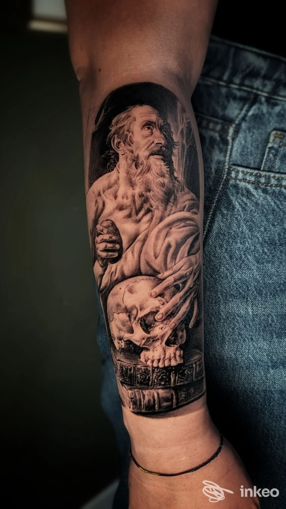 Tatuaggio realistico in bianco e nero sull'avambraccio con figura di vecchio barbuto e teschio — foto portfolio Sacrosanto Tattoo Torino, Torino.