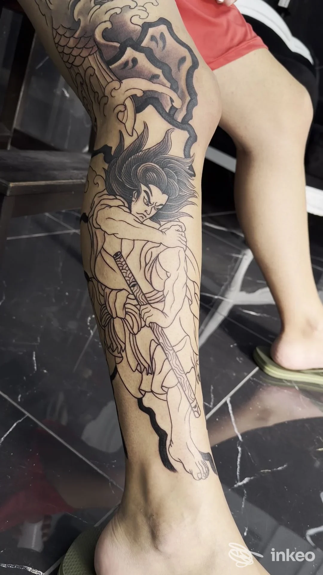 Tatuaggio in bianco e nero sul polpaccio raffigurante figura stilizzata con bastone, fotografia fornita da Ciko Tattoo Studio, Somma Vesuviana.