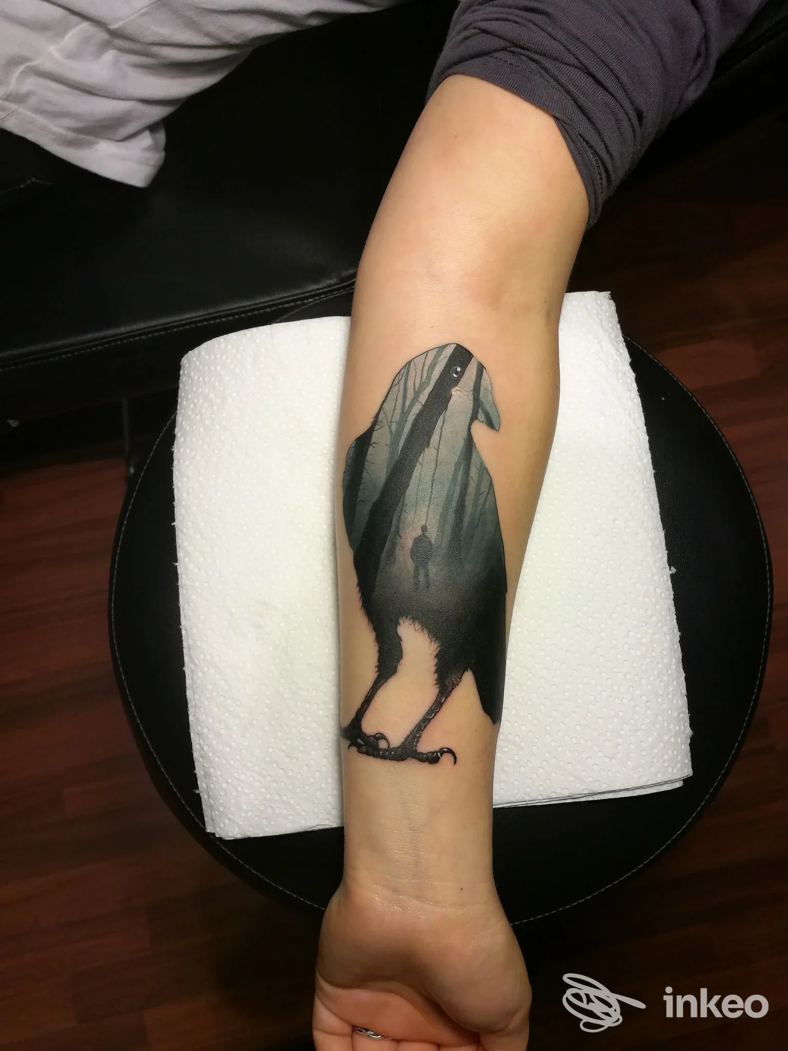 Tatuaggio a figura di corvo su avambraccio con paesaggio boschivo interno, fotografato nello studio Respect Tattoo a Stanghella.