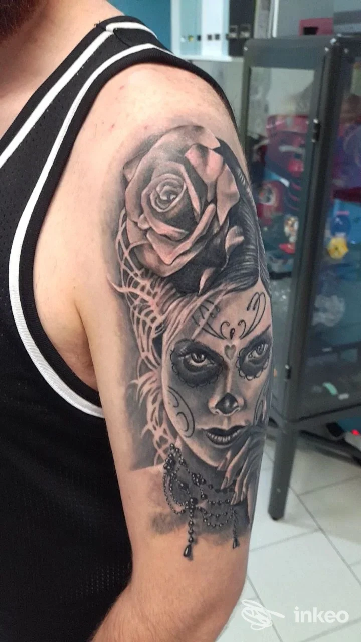 Tatuaggio black & grey su braccio superiore con rosa e volto in realismo, New Skin Tattoo, Copparo.