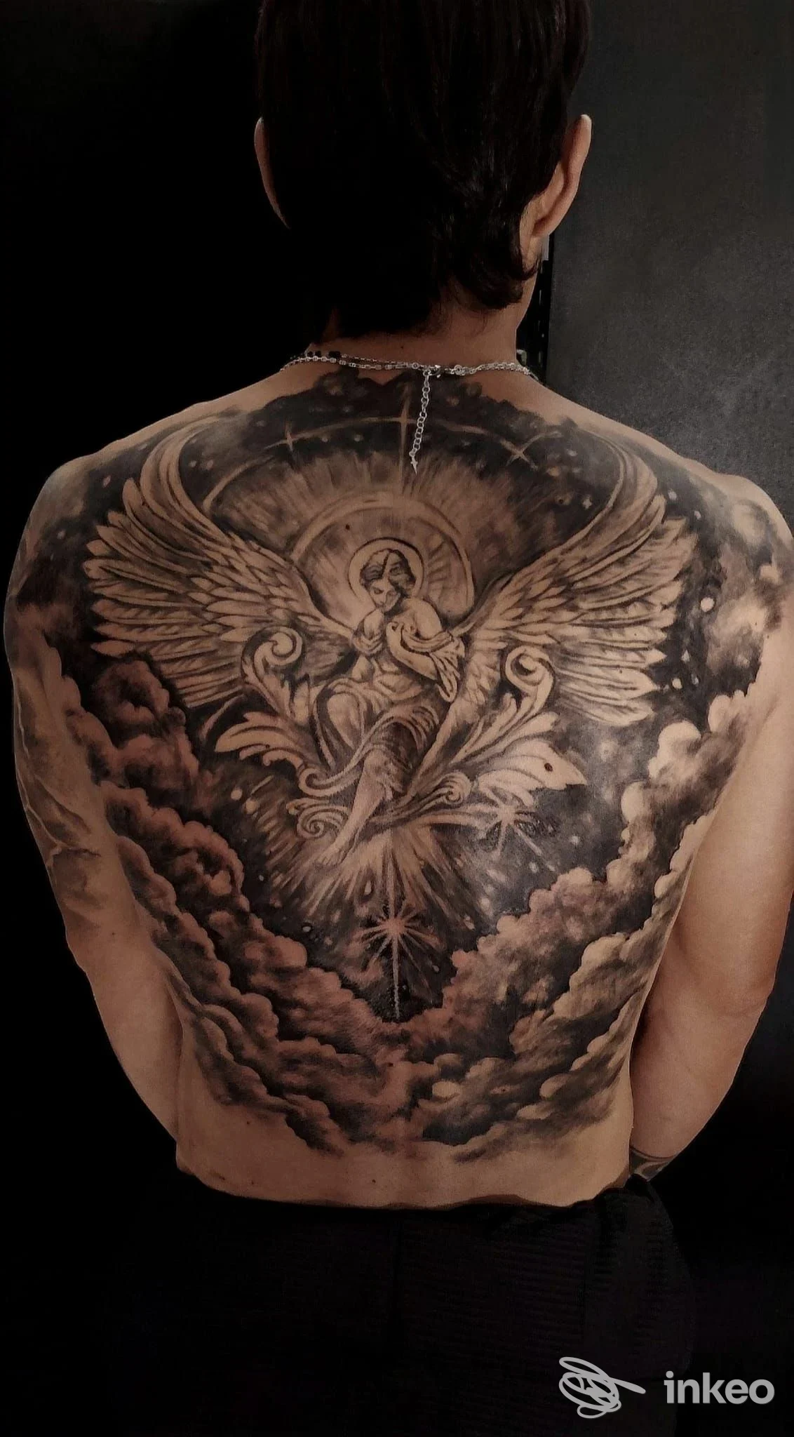 Ampia schiena tatuata con un angelo centrale tra ali spiegate e nubi, lavoro in bianco e nero. AILA TATTOO, Ispica.