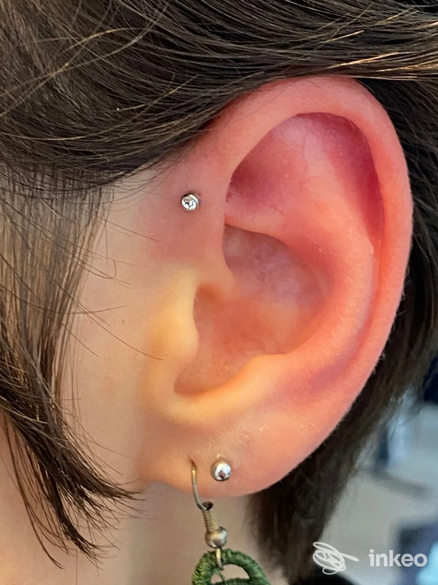 Piercing all'orecchio sinistro: due gioielli sull'orecchio, uno sull'elice e uno sullobo, con una piccola pietra chiara e una piccola anilla. Primo piano dell'orecchio senza viso completo.