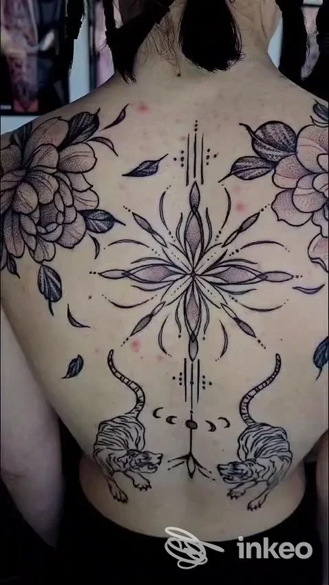 Tatuaggio ornamentale ampio sulla schiena con mandala centrale, fiori sulle spalle e due tigri in basso; immagine da ARI TATTOO PRATO, Montemurlo.