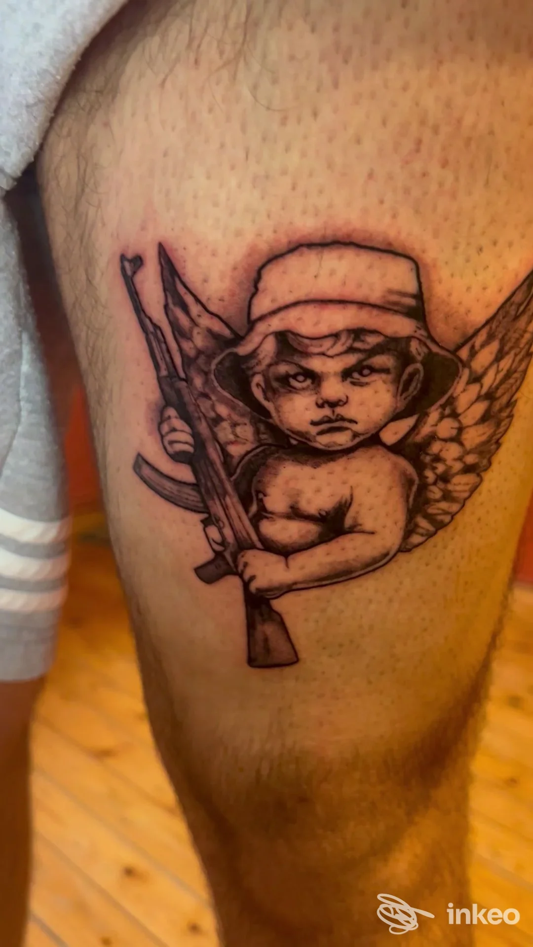 Tatuaggio su coscia raffigurante un cherubino alato con fucile, Lachiusa Tattoo Club, Casale Monferrato.