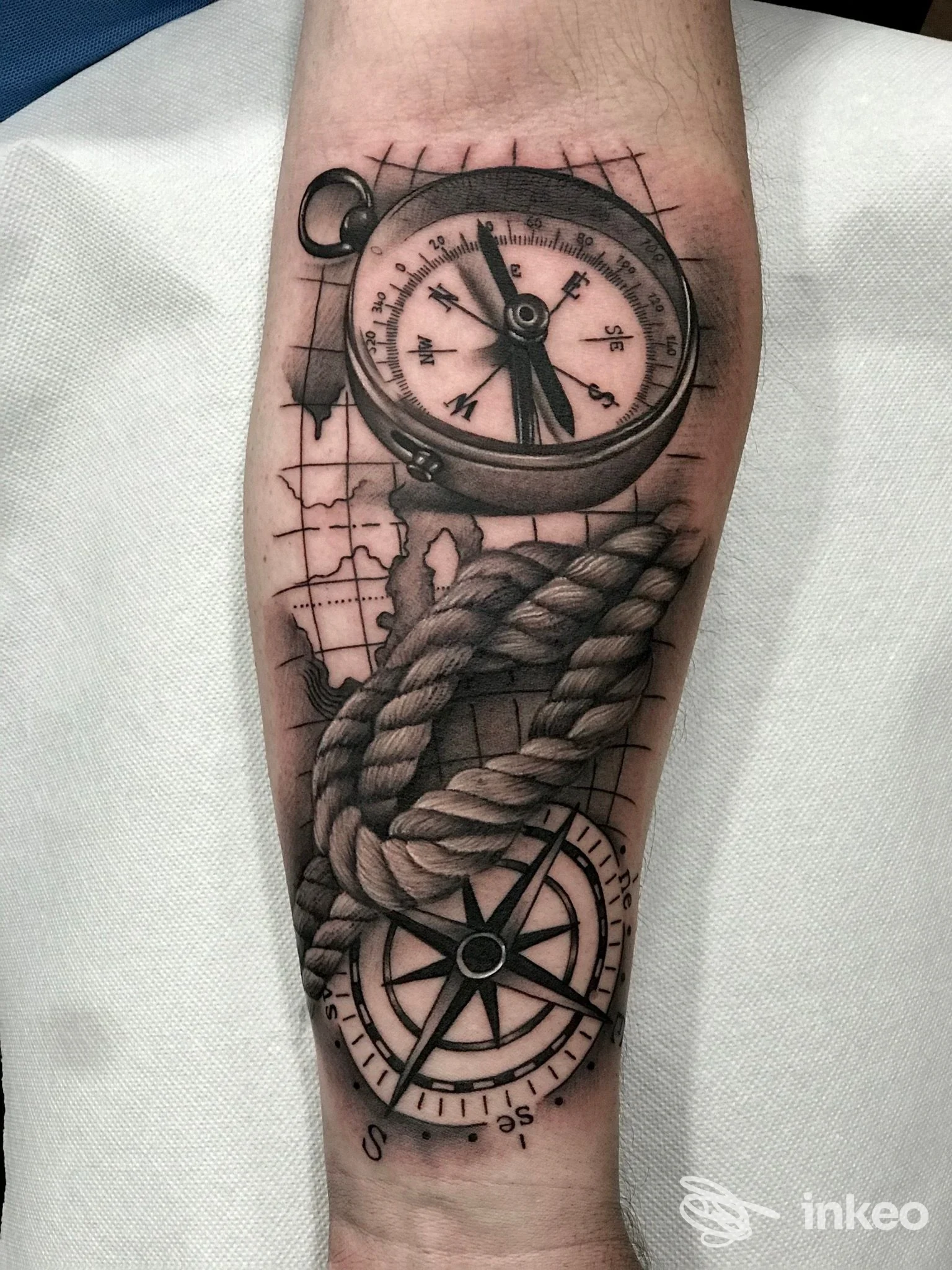 Tatuaggio realistico in bianco e nero su avambraccio con bussola, corda e mappa, foto da Black Owl Tattoo, Napoli.