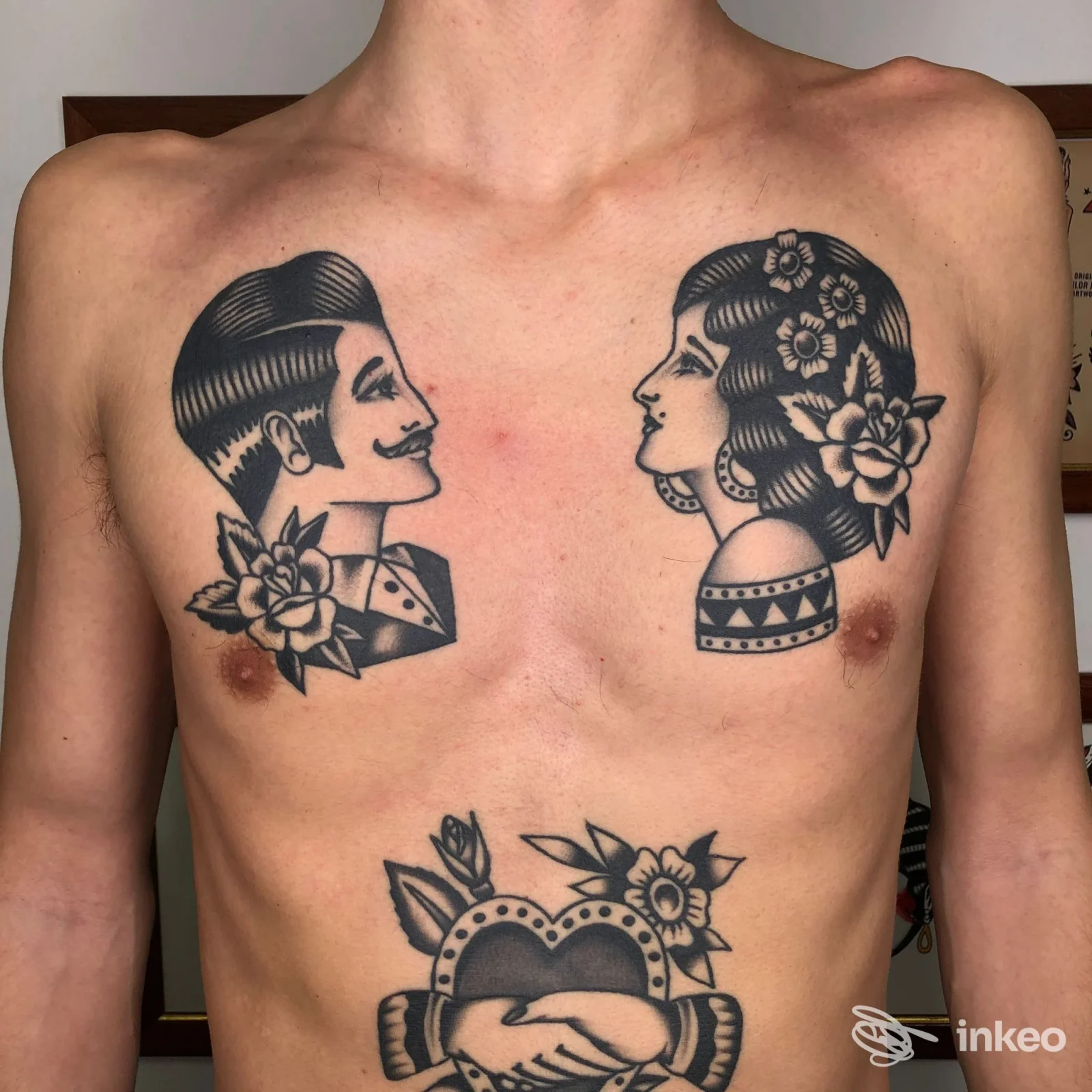 Torace di un soggetto senza camicia con due ritratti in stile tradizionale, accompagnati da fiori e un cuore decorato, tatuaggi ben definiti e in contrasto su pelle chiara.