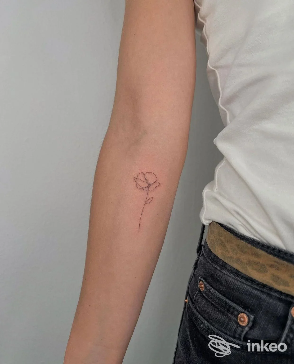Foto verticale di un avambraccio con un tatuaggio minimal a linea sottile raffigurante una rosa sull'avambraccio interno. Il trucco di Roby, Valenza.