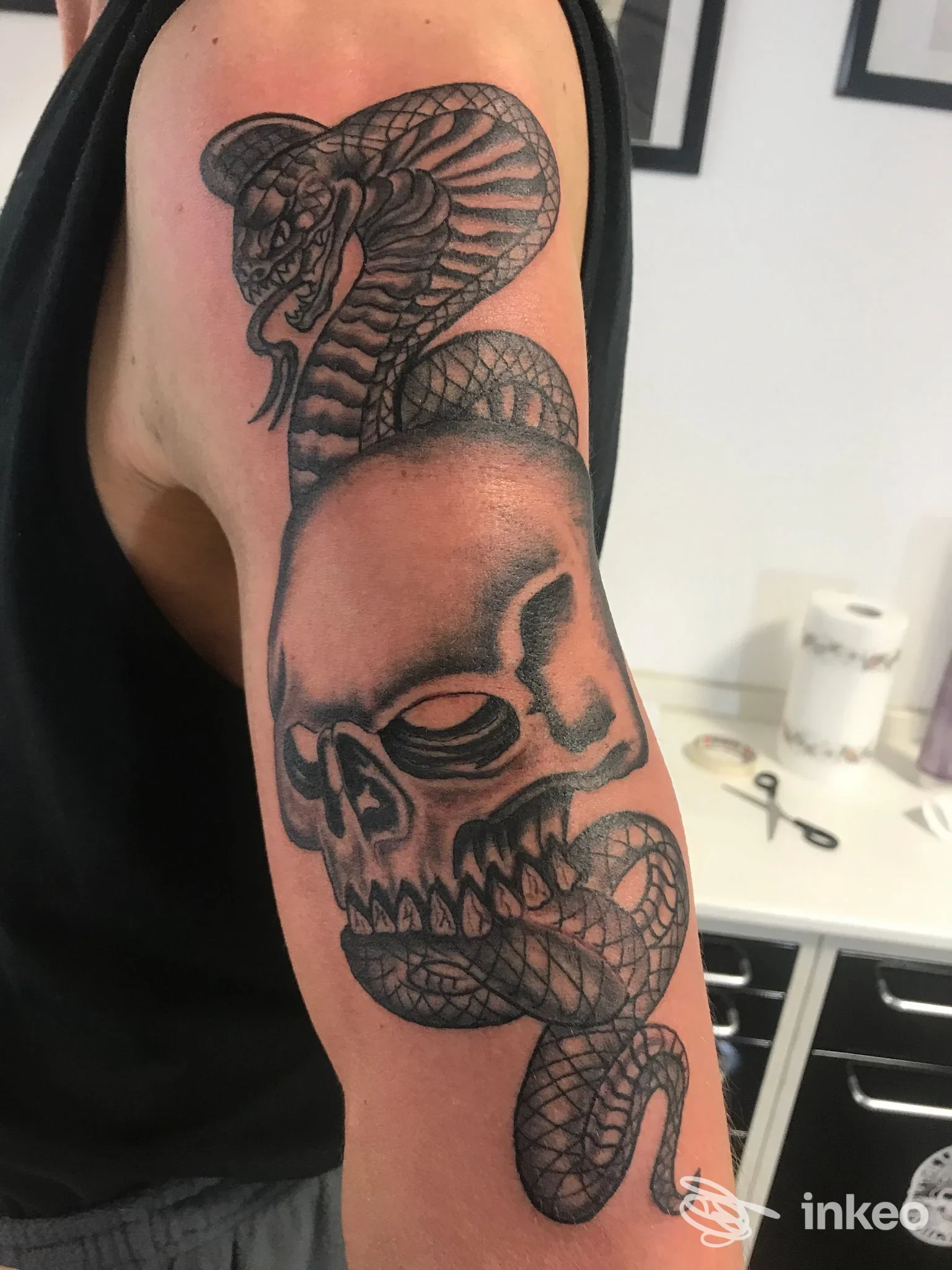 Tatuaggio black & grey su braccio superiore raffigurante un teschio avvolto da un cobra — Ink'n'Blood Tattoo, Forlì.