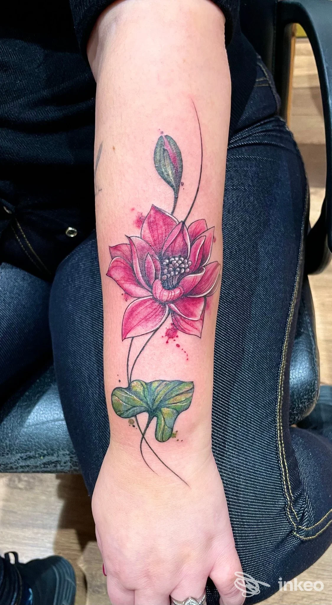 Tatuaggio a colori di un fiore di loto sull'avambraccio, petali rosa e foglia verde, fotografato nello studio DDT Tattoo a Cento.