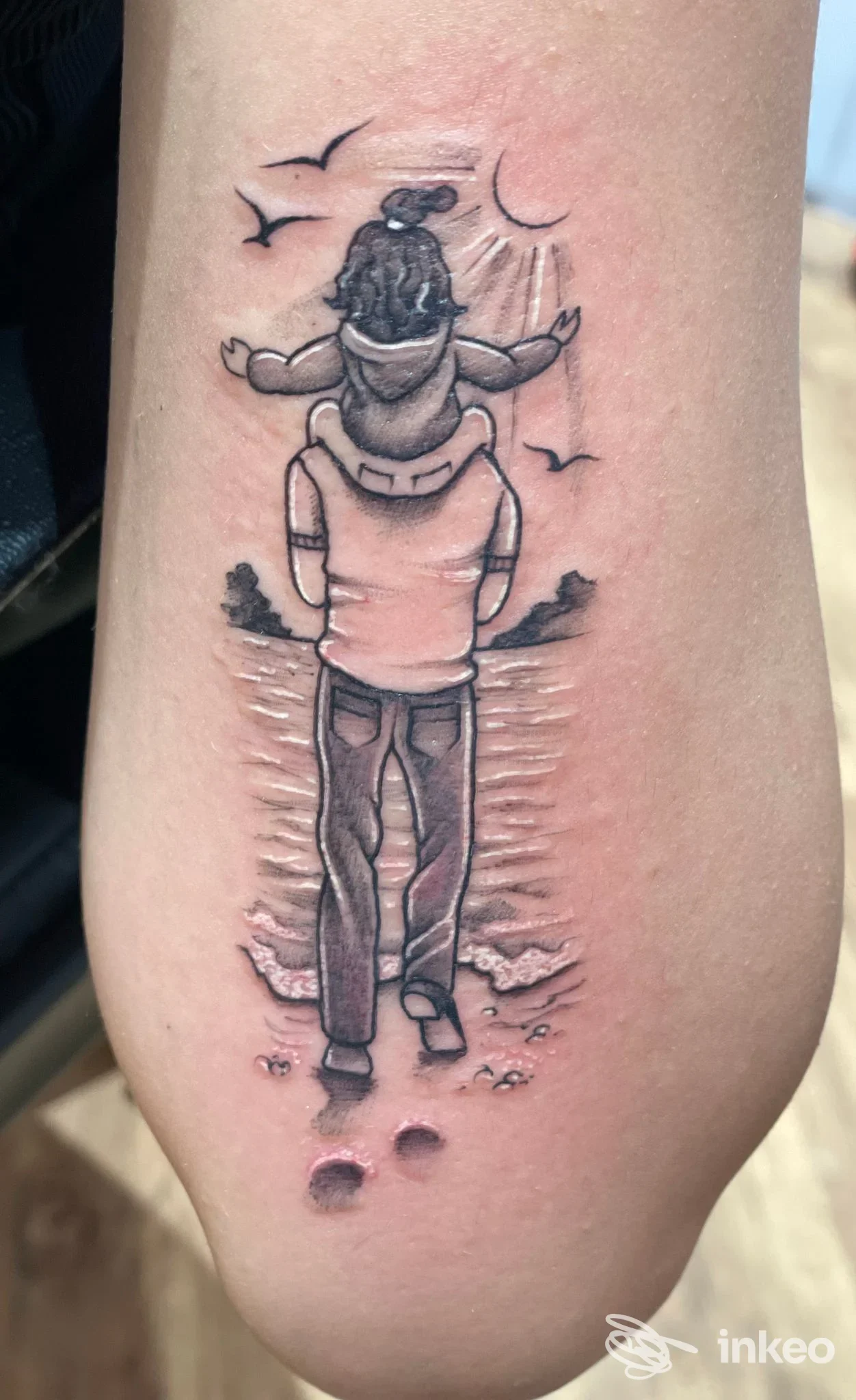 Tatuaggio black & grey su avambraccio raffigurante una figura con bambino in spalla davanti al mare - DDT Tattoo, Cento.