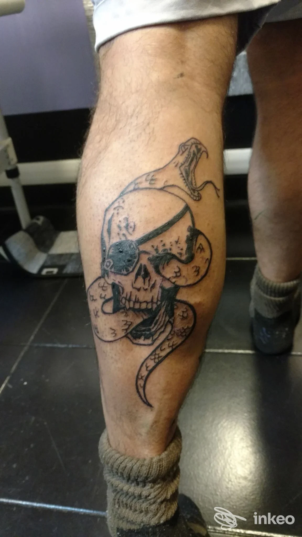 Tatuaggio su polpaccio che raffigura un teschio avvolto da un serpente, fotografato in studio; immagine fornita da Il Giglio Nero Tattoo a Campi Bisenzio.