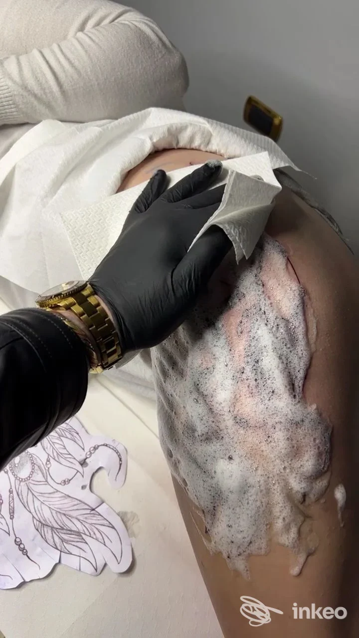 Tatuaggio in fase di pulizia sulla coscia, mano con guanto nero e disegno preparatorio visibile. GiòTattoos, Formia.