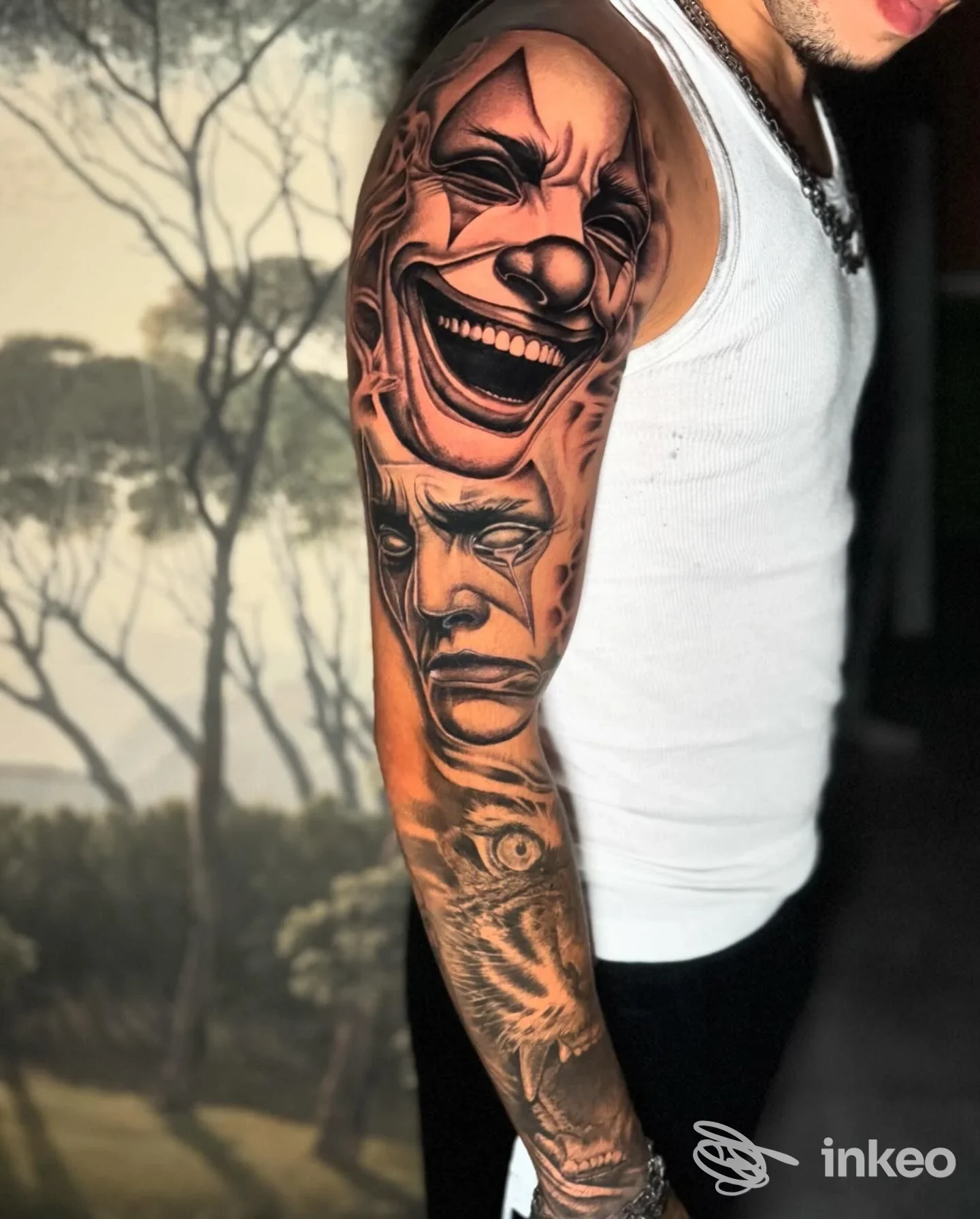 Tattoo visibile sull'avambraccio di un uomo: cloune sorridente in alto e volto stilizzato sotto, quasi a formare una scena verticale sul braccio, con maglietta bianca in sfondo.