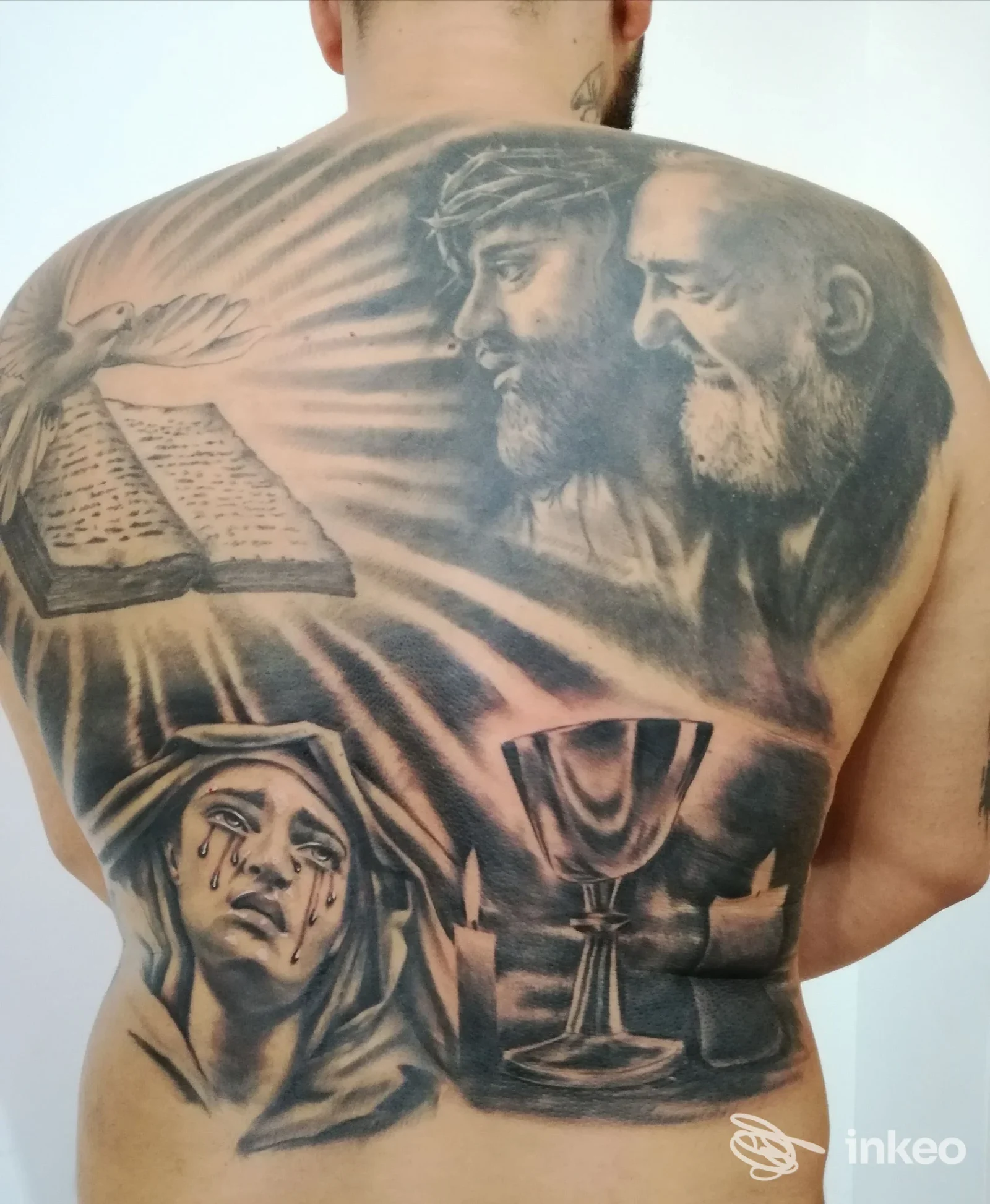 Grande tatuaggio religioso su tutta la schiena realizzato da Bodysigns Tattoos a Conversano, con volti e simboli sacri in bianco e nero.