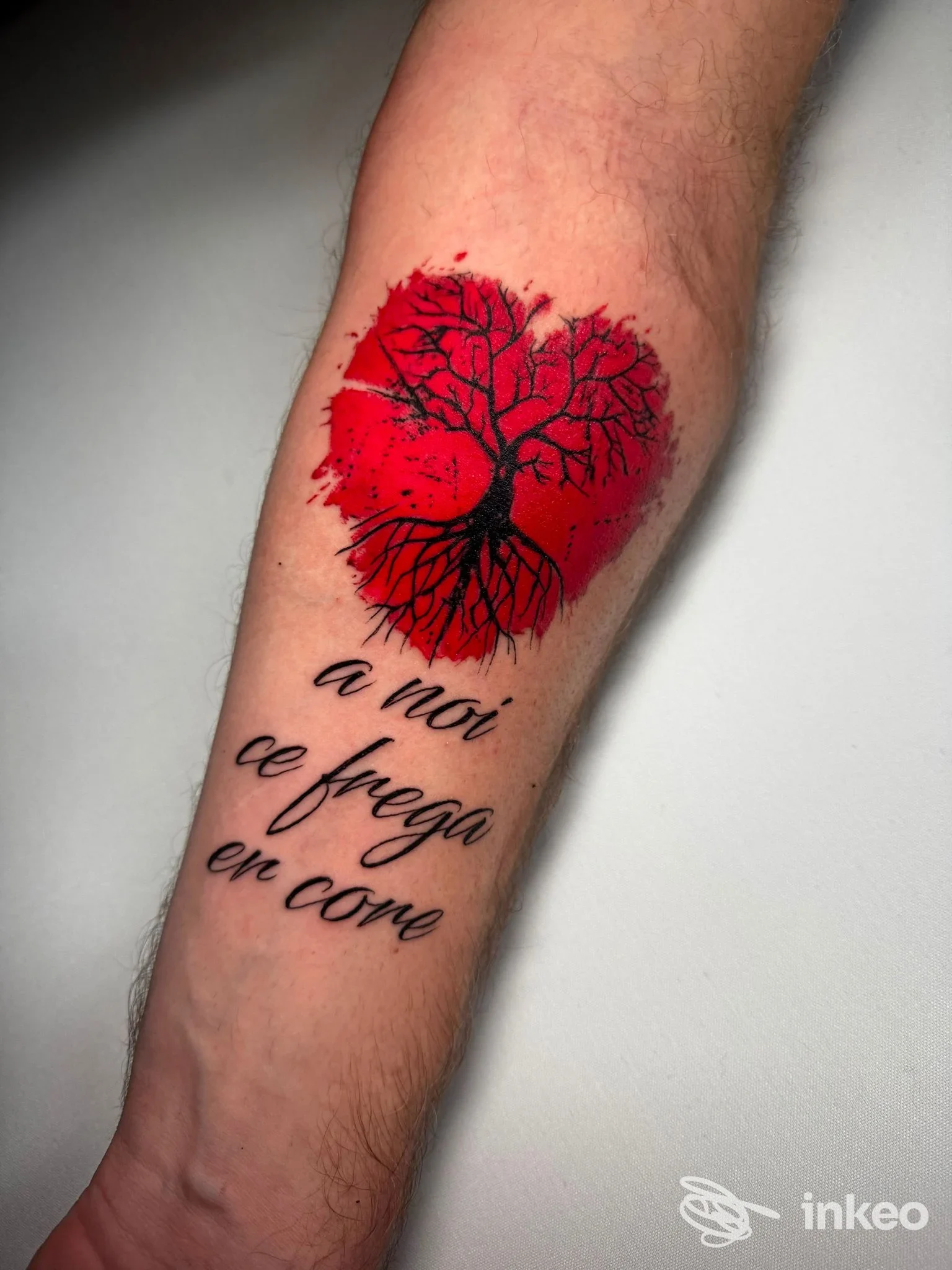 Tatuaggio a forma di cuore rosso con albero nero e testo in corsivo sull'avambraccio interno. BR1 INK Tattoo & Piercing, Guidonia Montecelio.