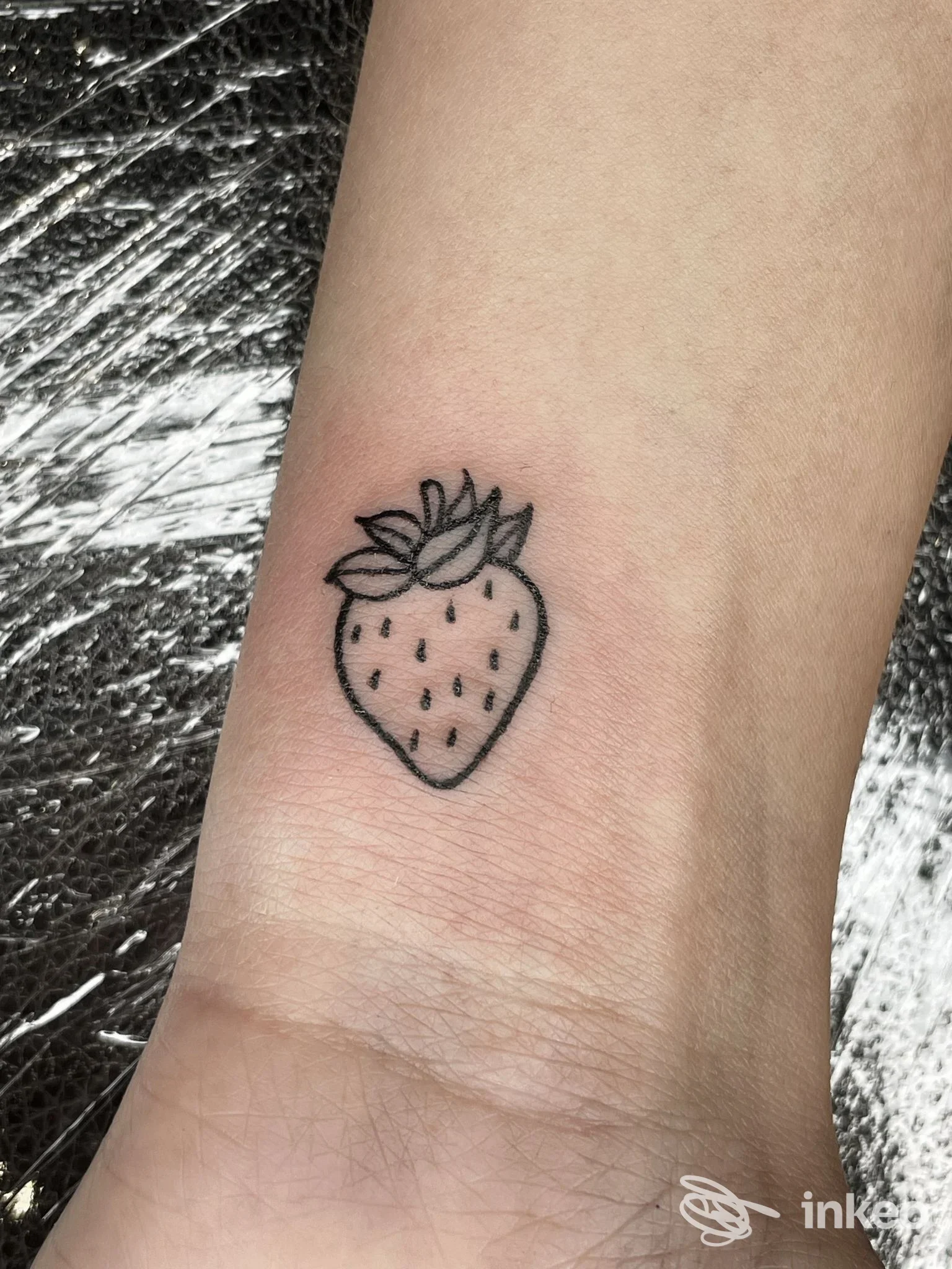 Piccolo tatuaggio a forma di fragola sul polso, foto di Marblueyes Tattoo a Cuneo che mostra il tratto in nero su pelle.