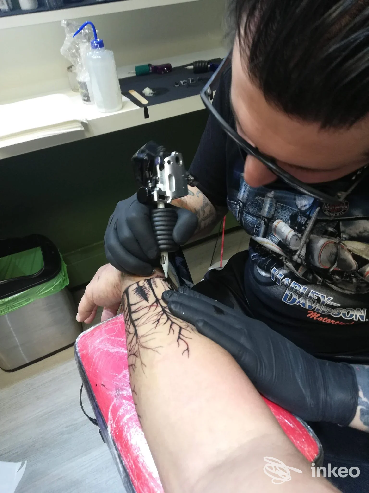 Operatore con guanti realizza un tatuaggio su gamba con disegno vascolare, in studio, utilizzando una macchina per tatuaggio.