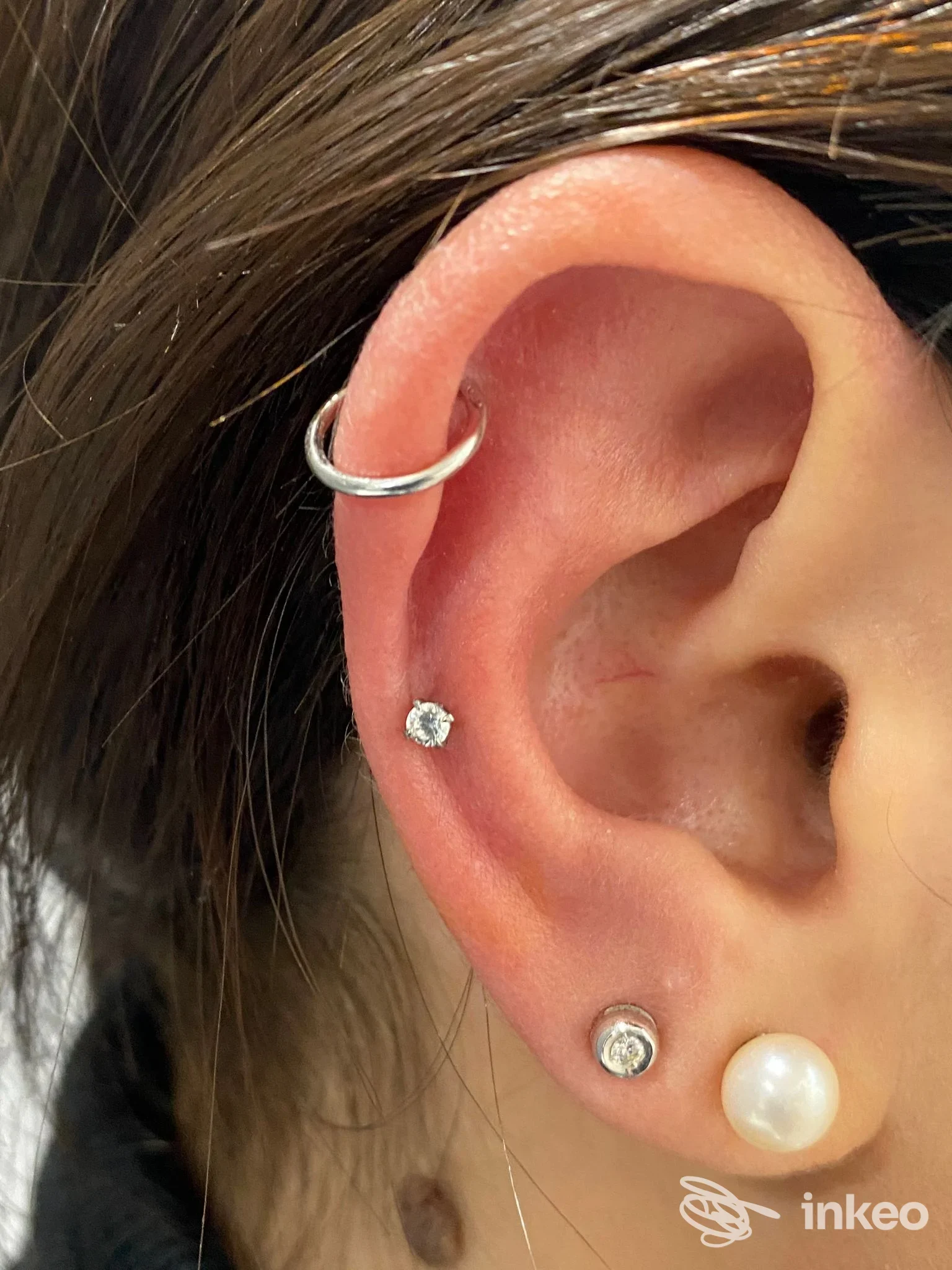 Primo piano di un orecchio con tre piercing (helix, tragus/padiglione e due lobi) - Nina Rock Ink Tattoo & piercing studio, Aprilia.