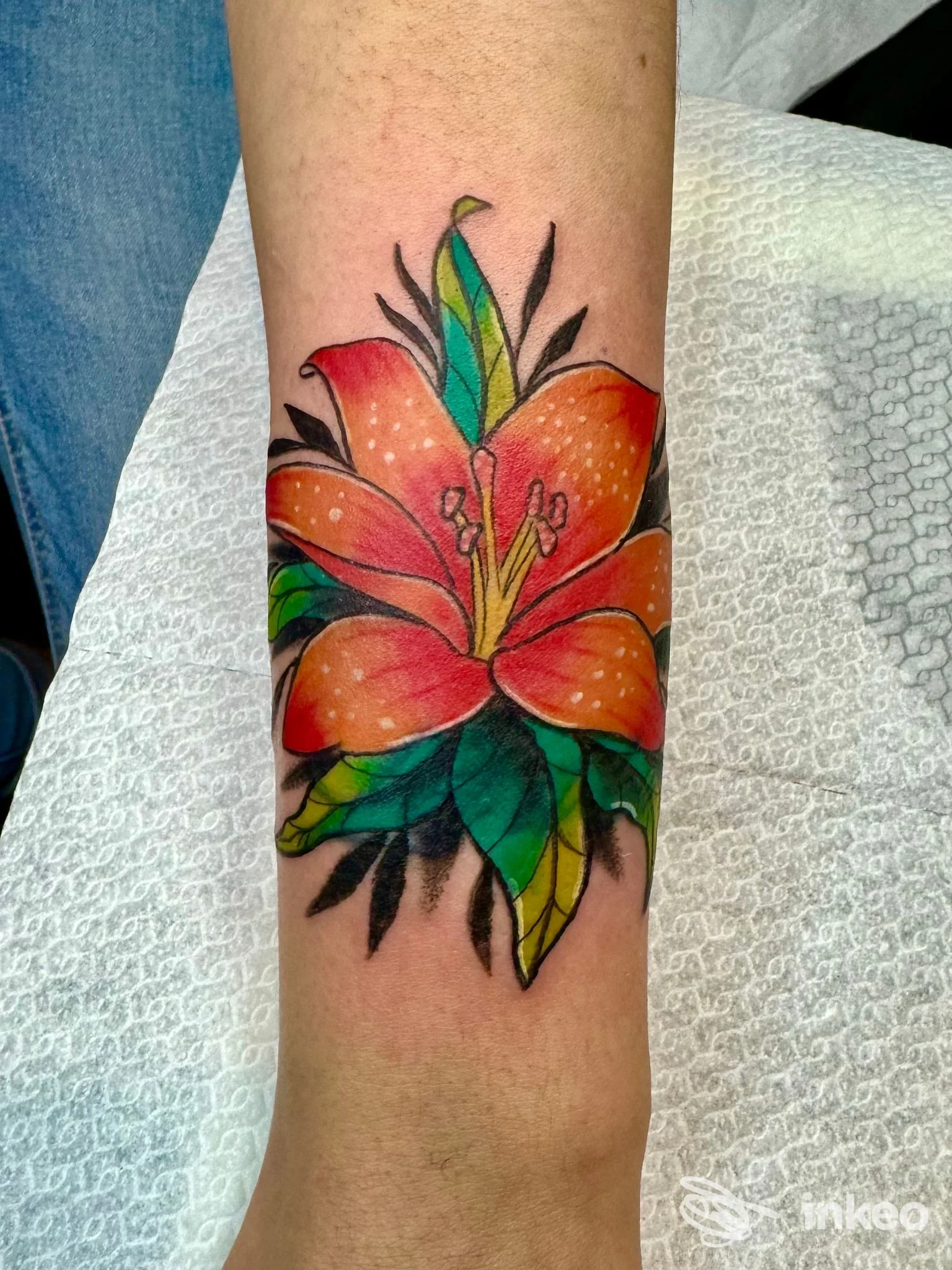 Tatuaggio floreale colorato su avambraccio realizzato da BLACK FLAG TATTOO, Riano: giglio arancione con foglie verdi su pelle reale.