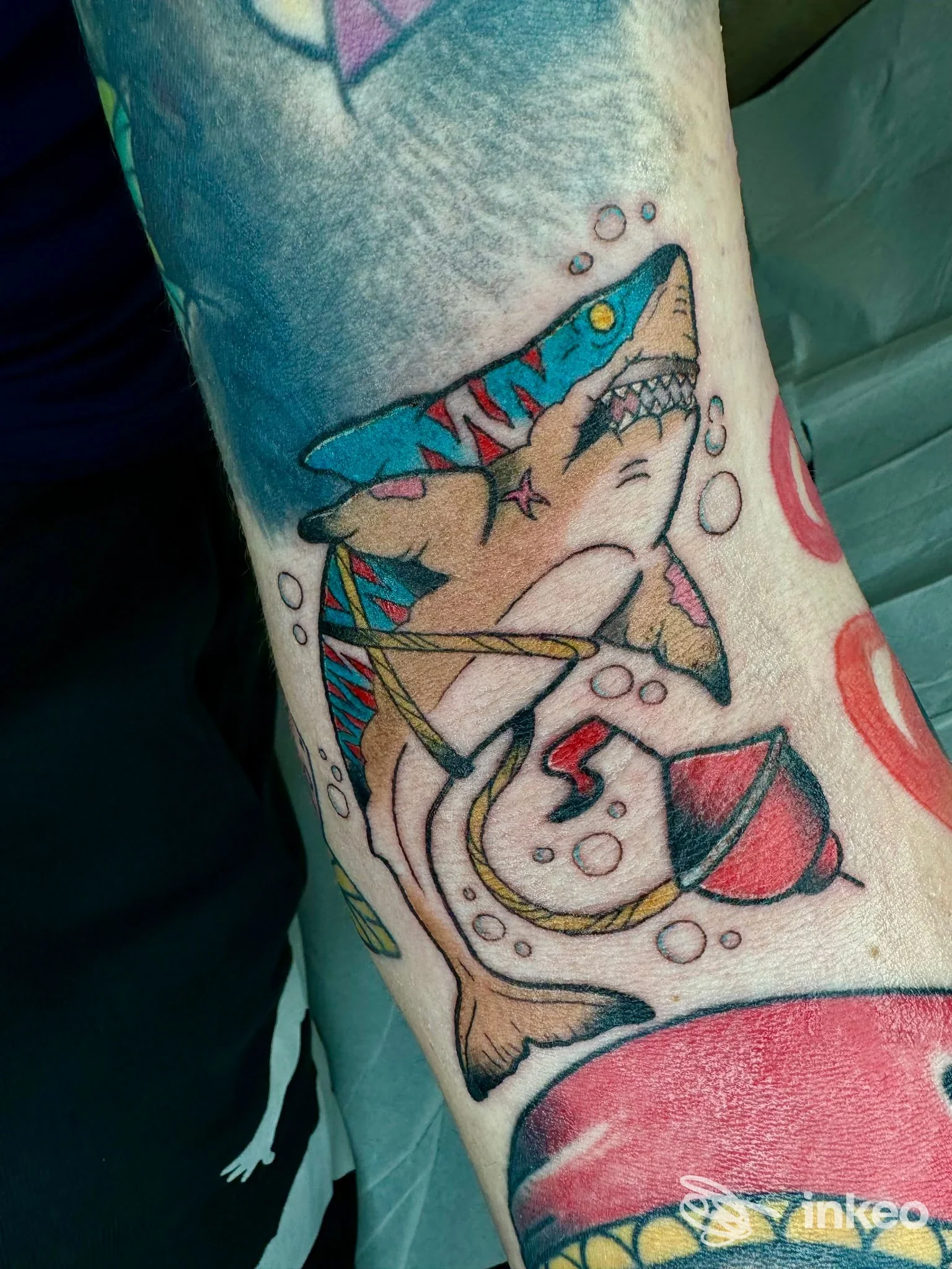 Tatuaggio di uno squalo colorato con boa e bolle sull'avambraccio, foto fornita da BLACK FLAG TATTOO a Riano.