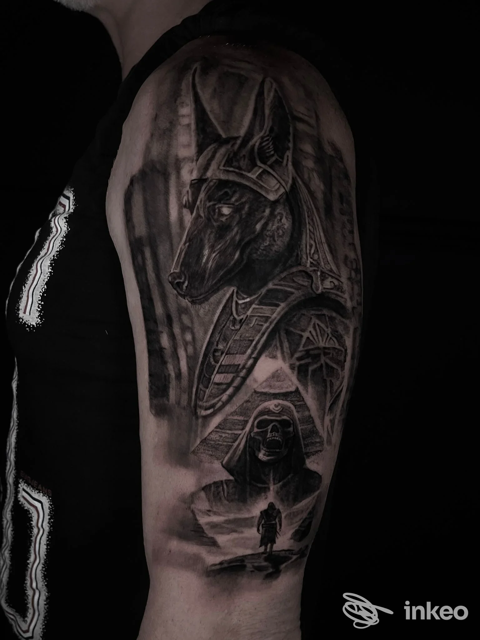Tatuaggio realistico sul braccio superiore raffigurante figure ispirate all'iconografia egizia. UNDERDOG TATTOO, Castel di Lama.