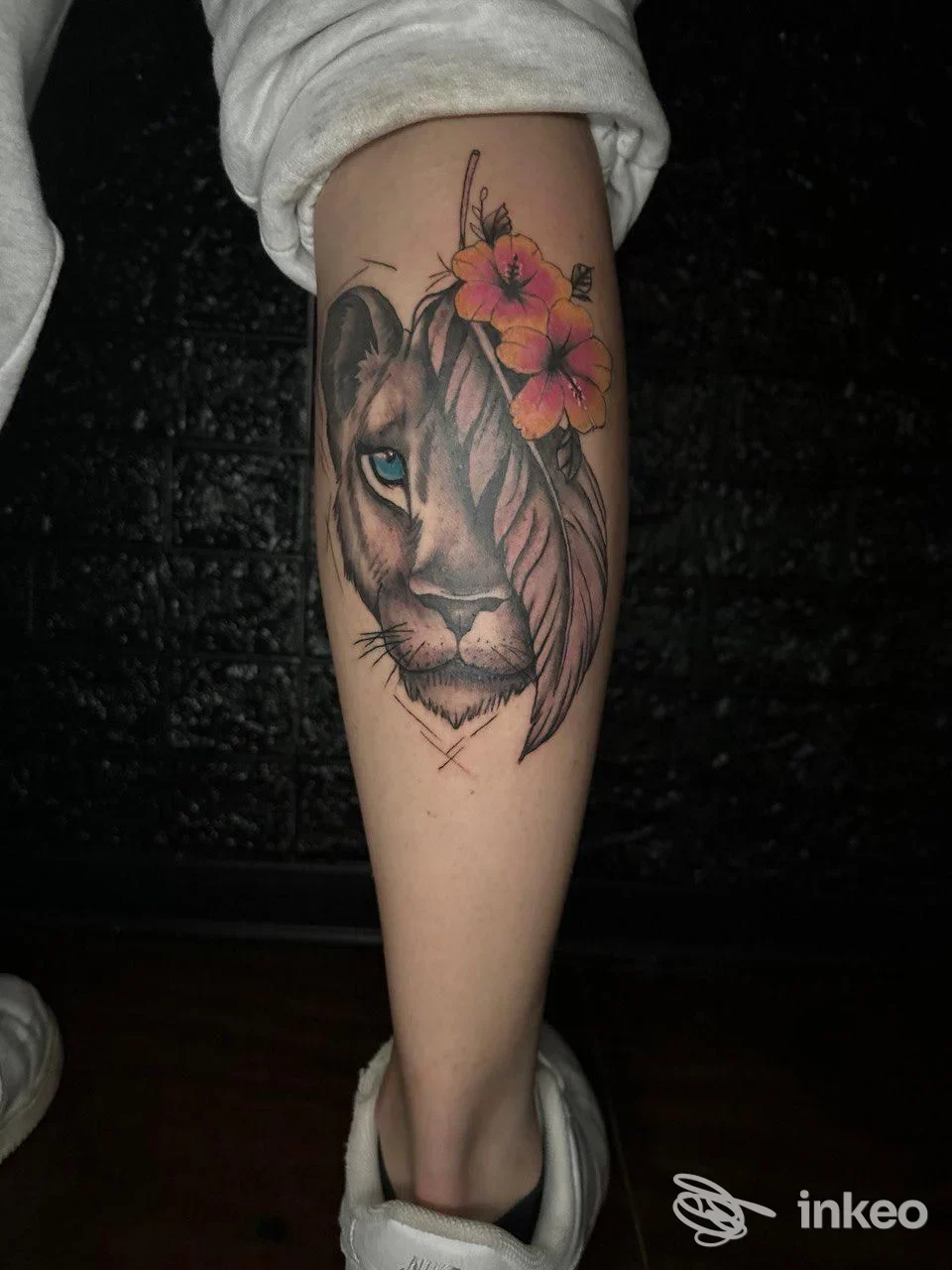 Tatuaggio sul polpaccio raffigurante volto di leonessa parziale con foglie e fiori colorati, lavoro di Valkiria Tattoo a Nettuno.