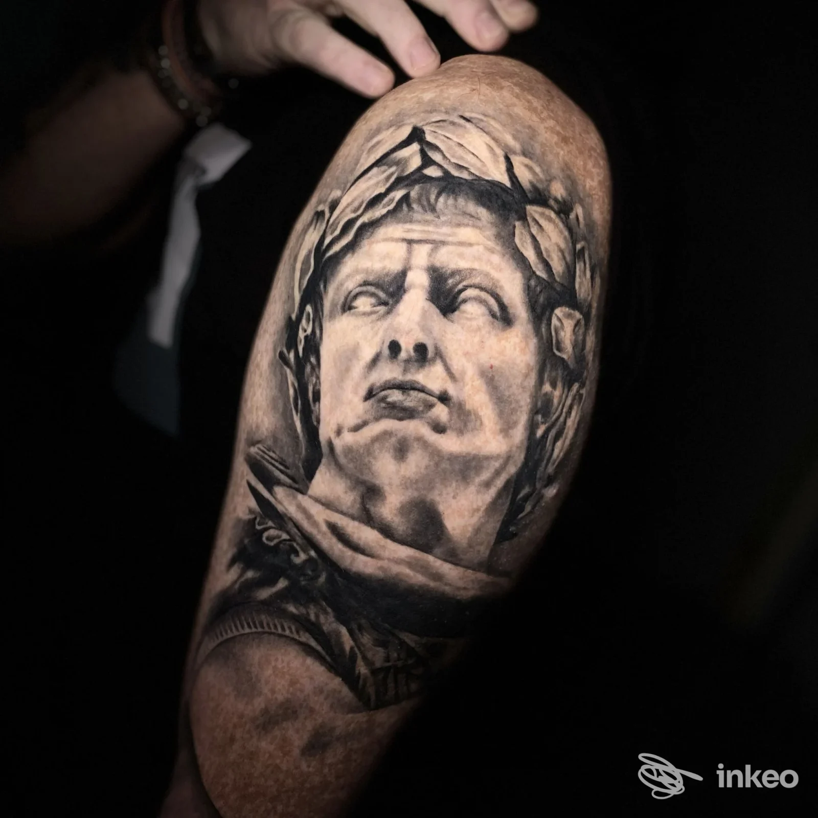 Tatuaggio realistico in bianco e nero raffigurante un volto scultoreo sulla parte superiore del braccio, fotografia del lavoro, End8_tattoo, Novi Ligure.