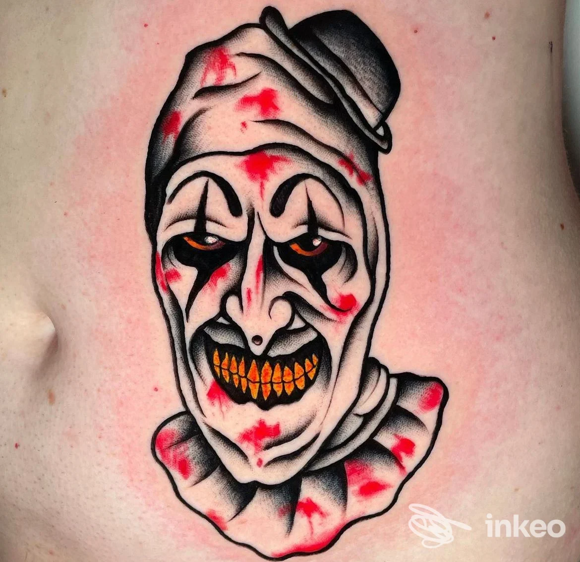 Tatuaggio su fianco/addome raffigurante un volto di clown in nero, rosso e giallo. Bright and Bold Tattoo Studio, Tortona.