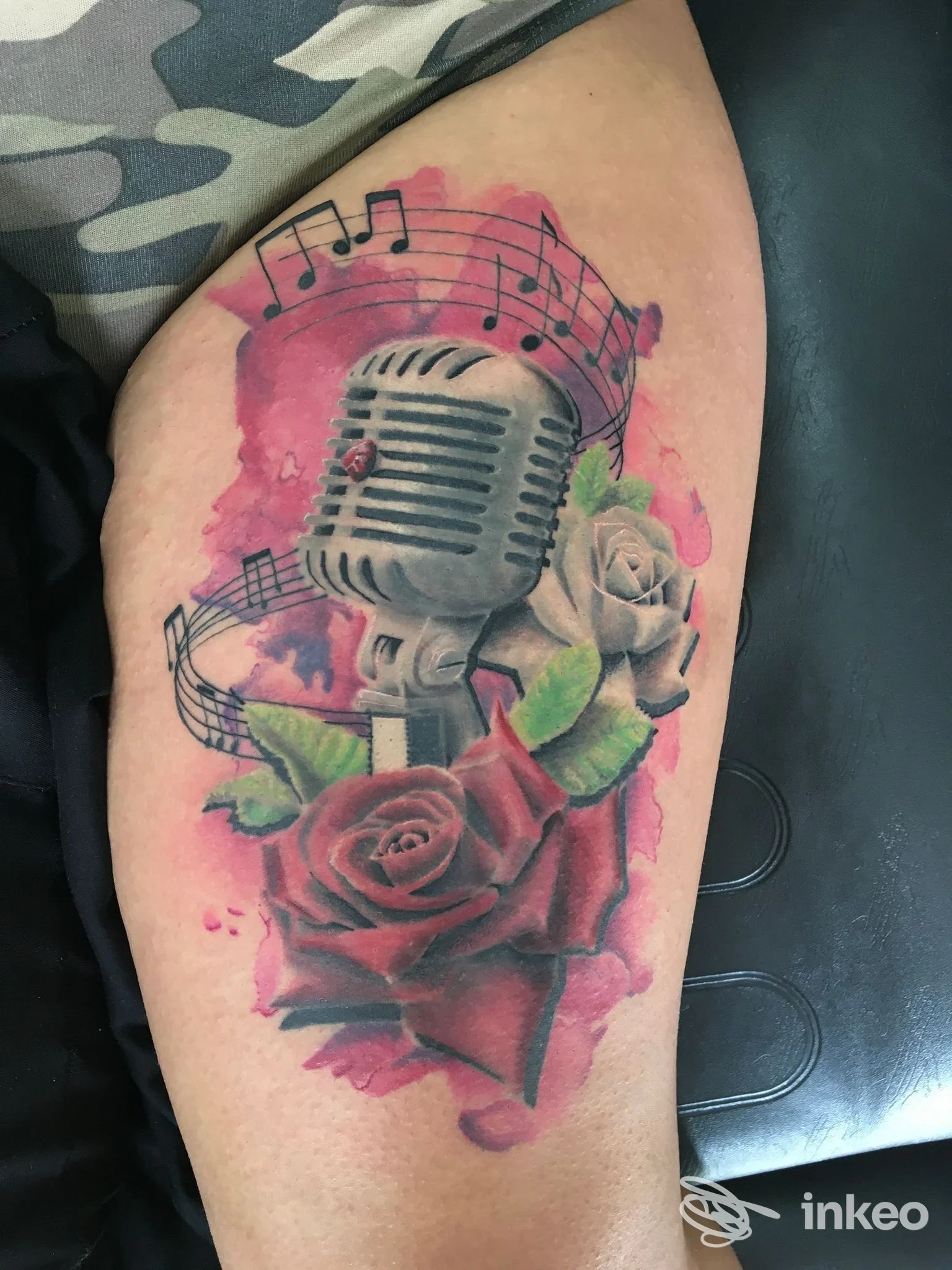 Tatuaggio su coscia con microfono vintage, rose e note musicali su sfondo rosa, NEED tattoo shop Novellara.