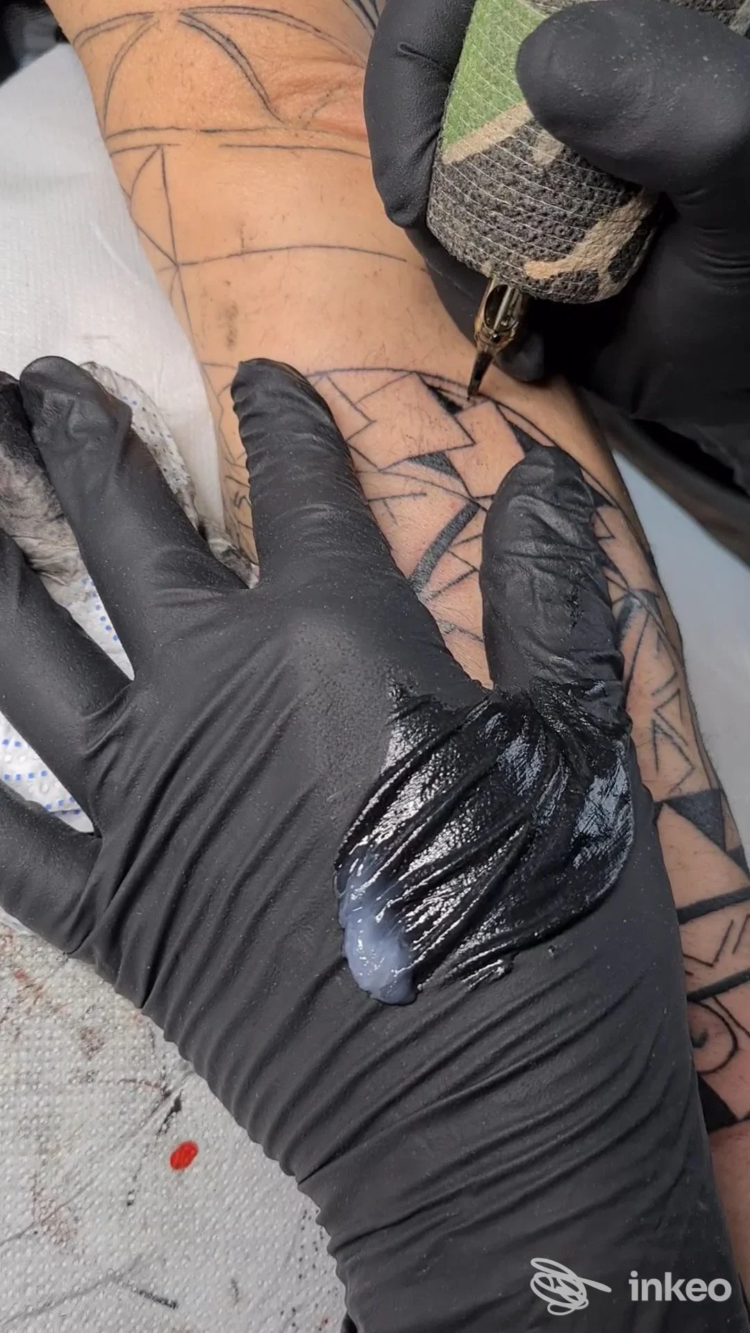 Primo piano di seduta tattoo su avambraccio con disegno geometrico; operatore con guanti neri e macchina in azione, All Ink Tatoo, Alessandria.