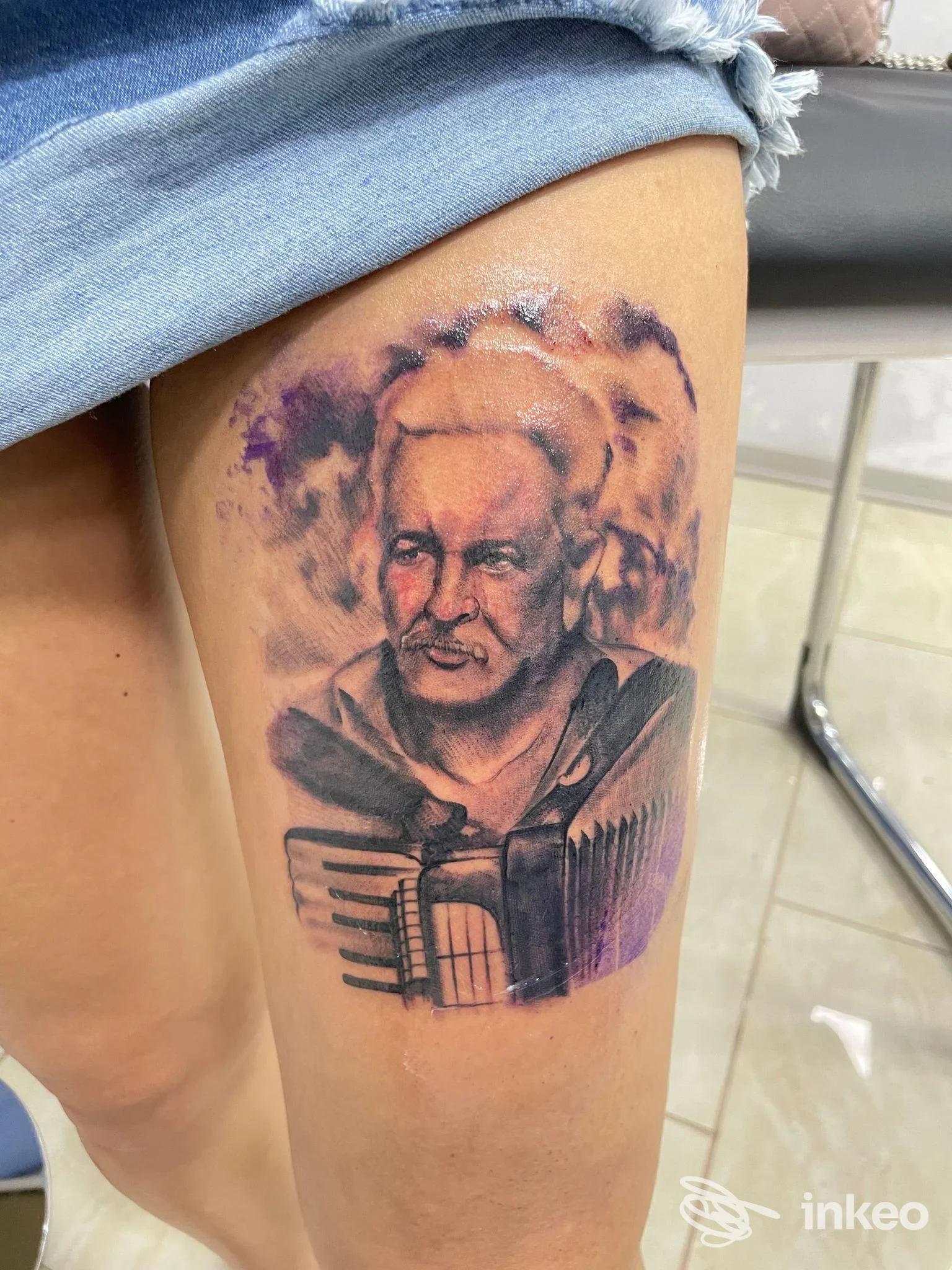 Tatuaggio realistico di un ritratto con fisarmonica sulla coscia, fotografato su pelle reale; immagine fornita dallo studio HADES TATTOO SHOP, Cassino.
