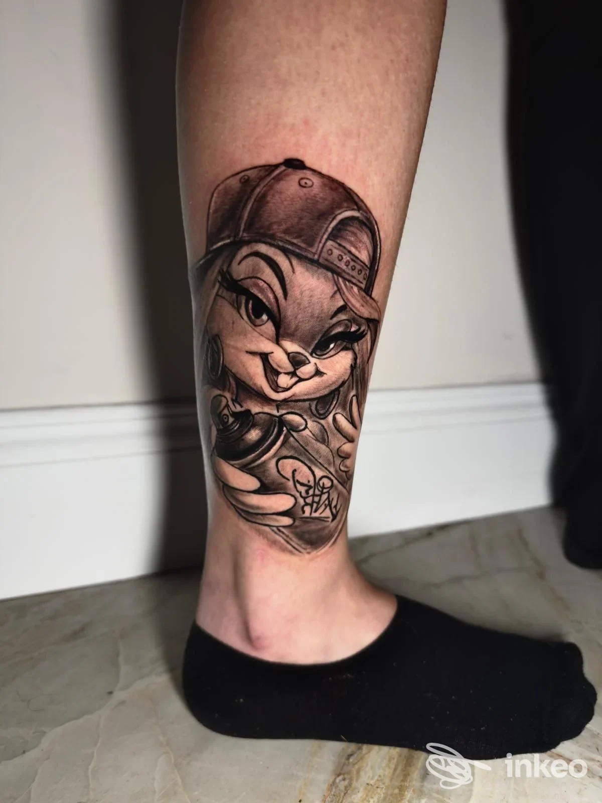 Tatuaggio in bianco e nero con personaggio cartoon sul polpaccio, immagine fornita da Esse27tattoo ad Anagni.