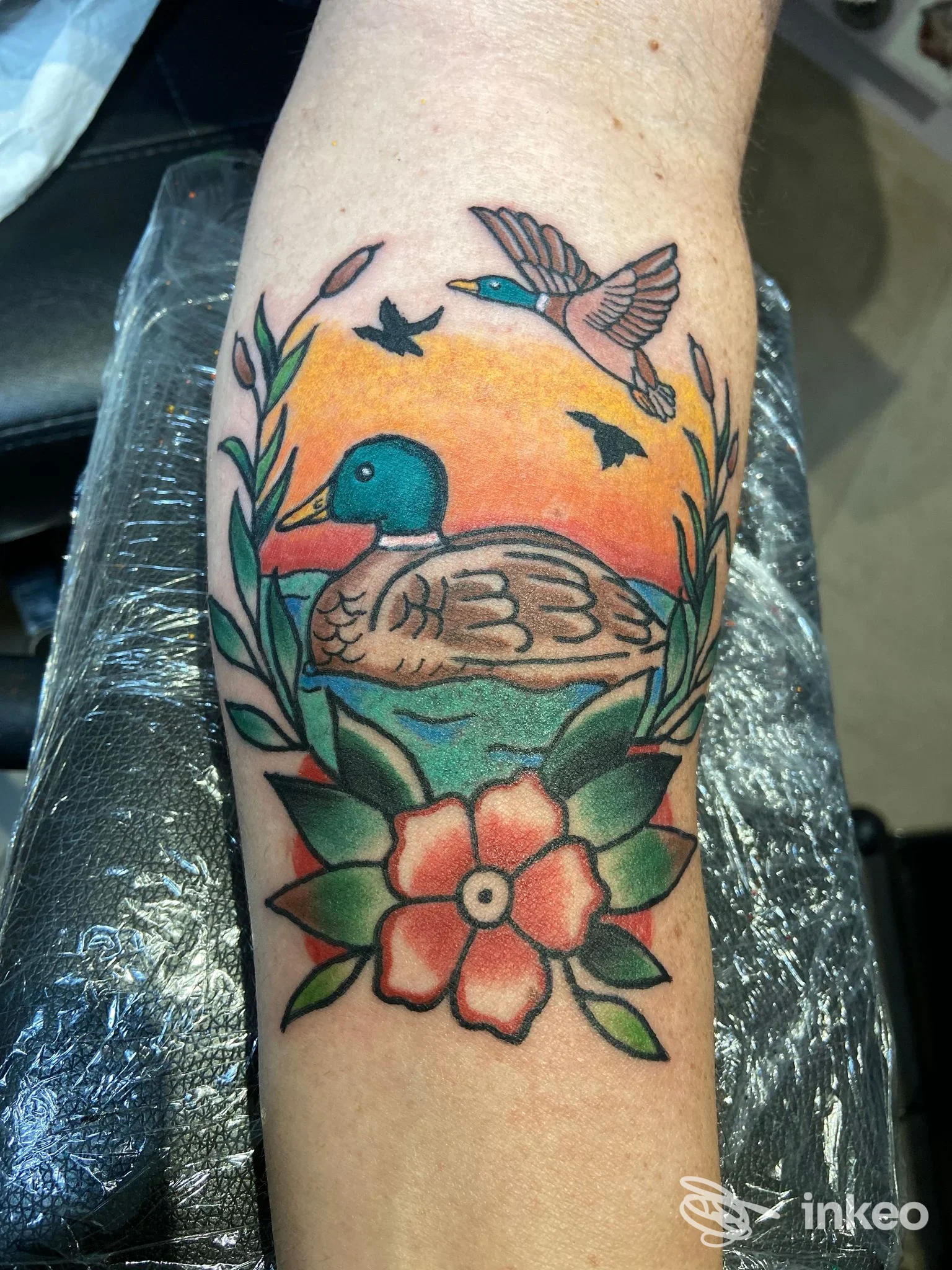 Tatuaggio tradizionale su avambraccio con anatra su acqua, cielo arancione e fiore stilizzato – Sweet Tattoo and Piercing, Sant'Ambrogio di Valpolicella.