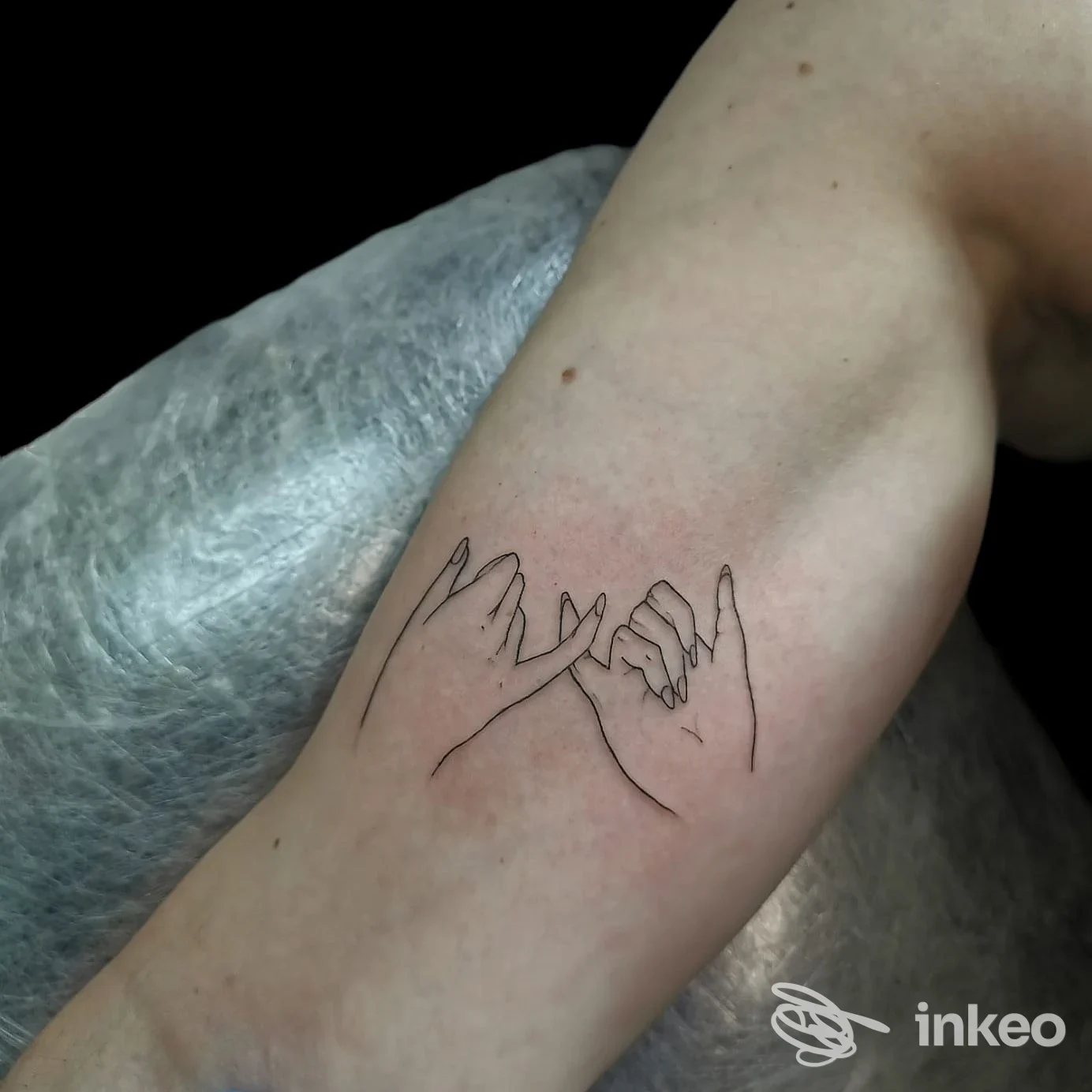 Tattoo lineare raffigurante due mani che si sfiorano sull'avambraccio, realizzato sulla pelle e visibile senza visi o testo, dentro studio in controluce.