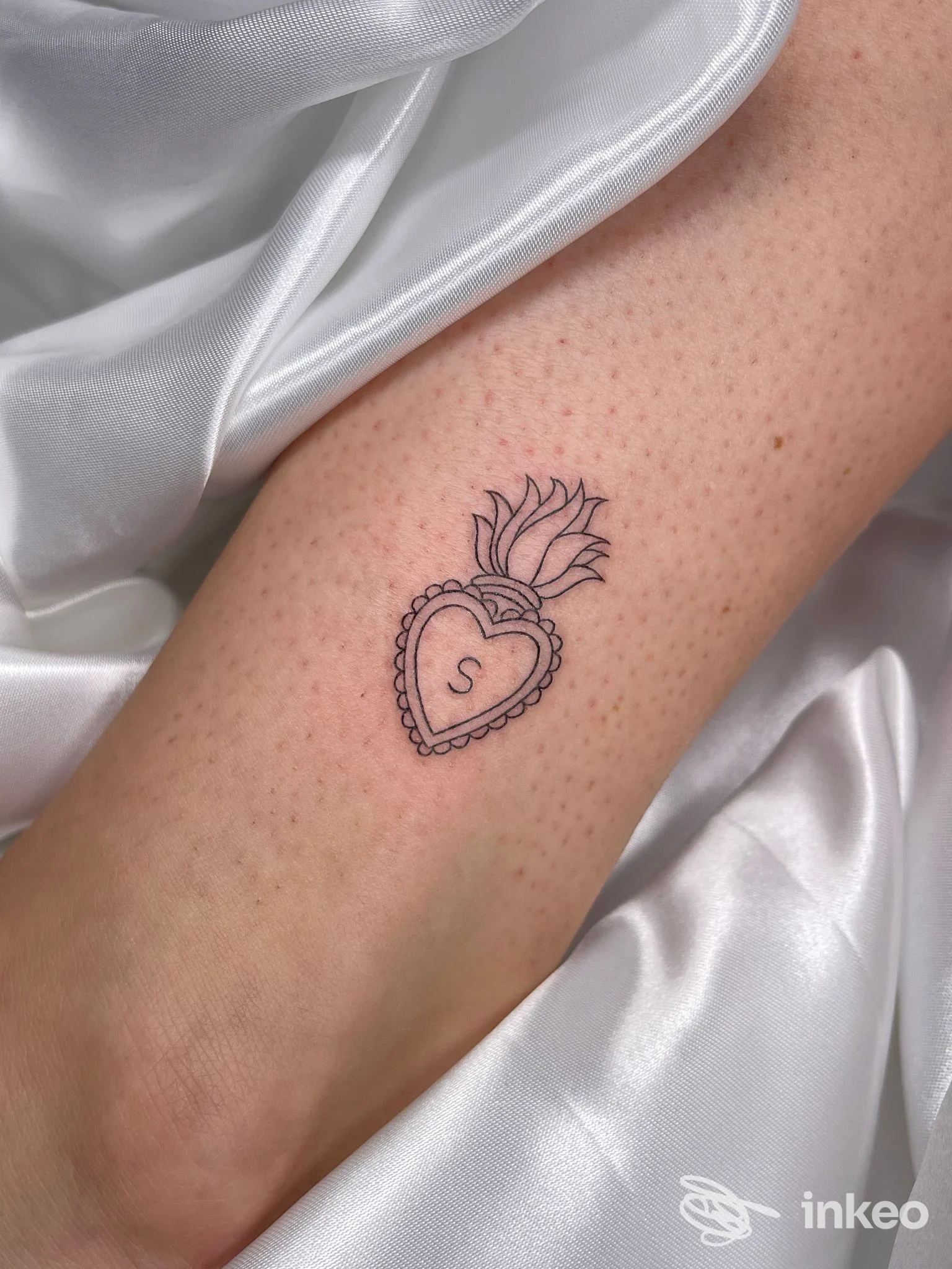 Piccolo tatuaggio a linee fini di un cuore sacro con iniziale 'S' sull'avambraccio interno — AMA.TE Tattoo Studio, Villafranca di Verona.