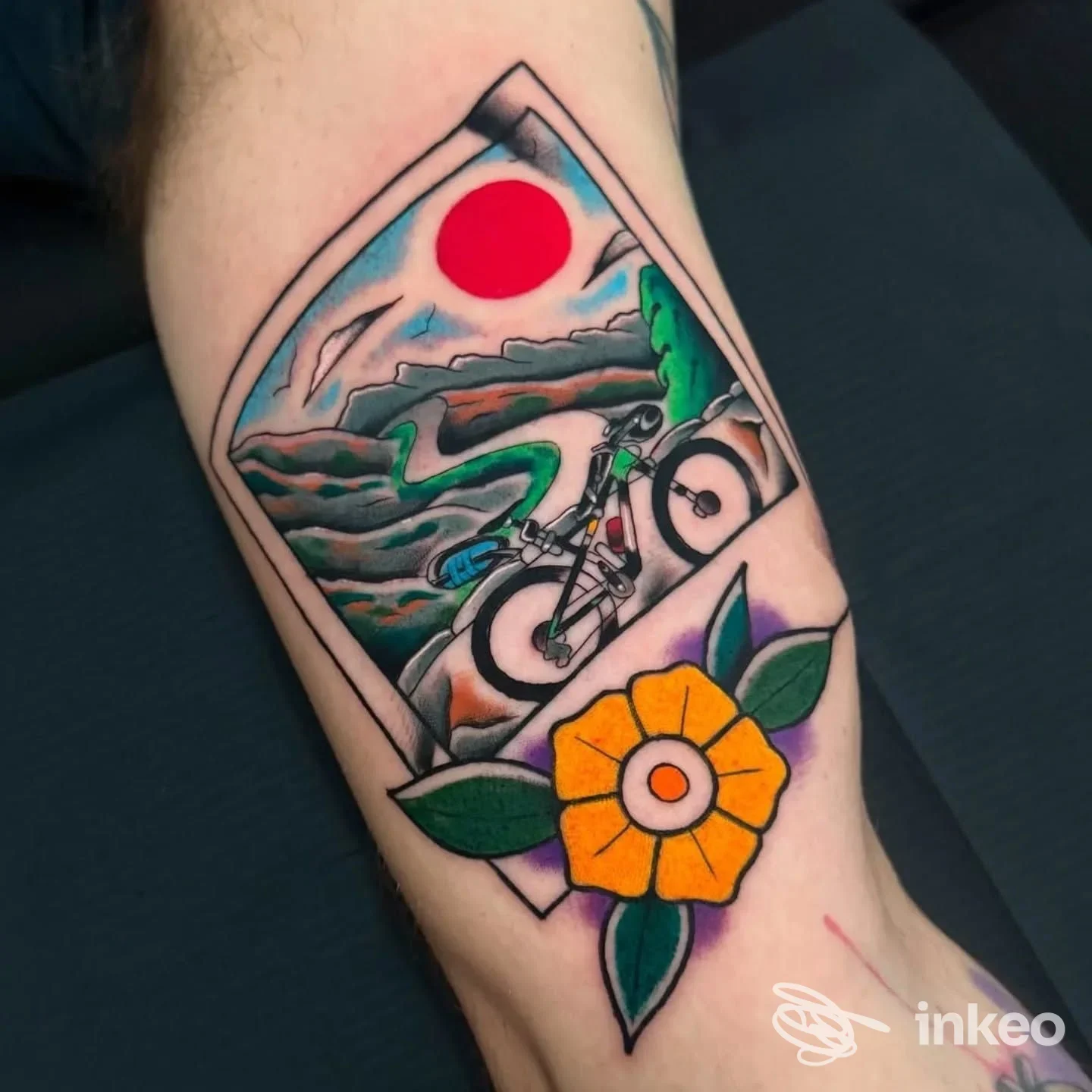Tattoo sul polpaccio raffigurante una scena con bici su un paesaggio montano incorniciato, accompagnata da un fiore giallo con foglie verdi, realizzato sulla pelle a Milano.