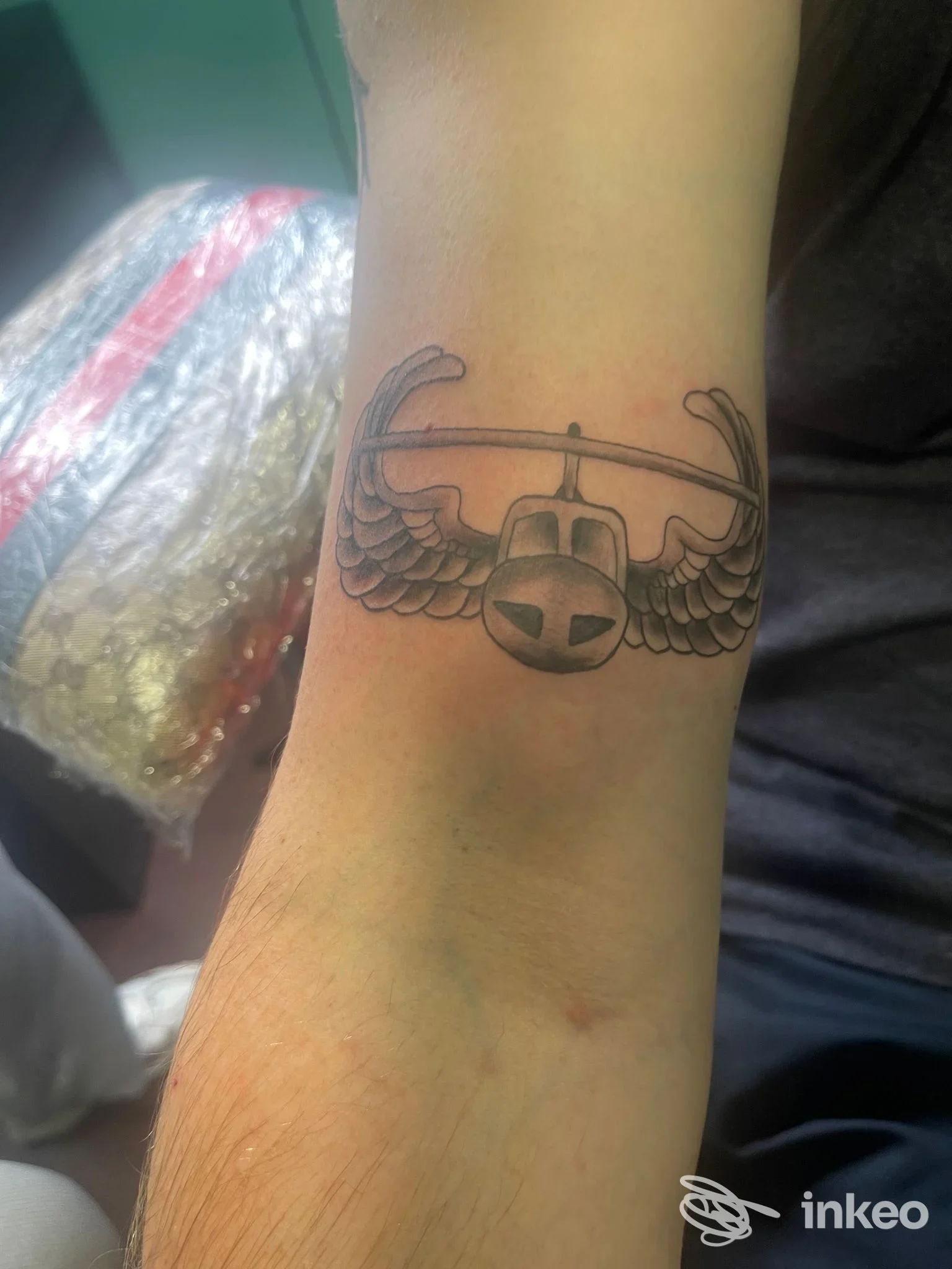 Tatuaggio sull'avambraccio di un aereo stilizzato con ali spiegate, fotografato nello studio La Industria INK a Taranto.