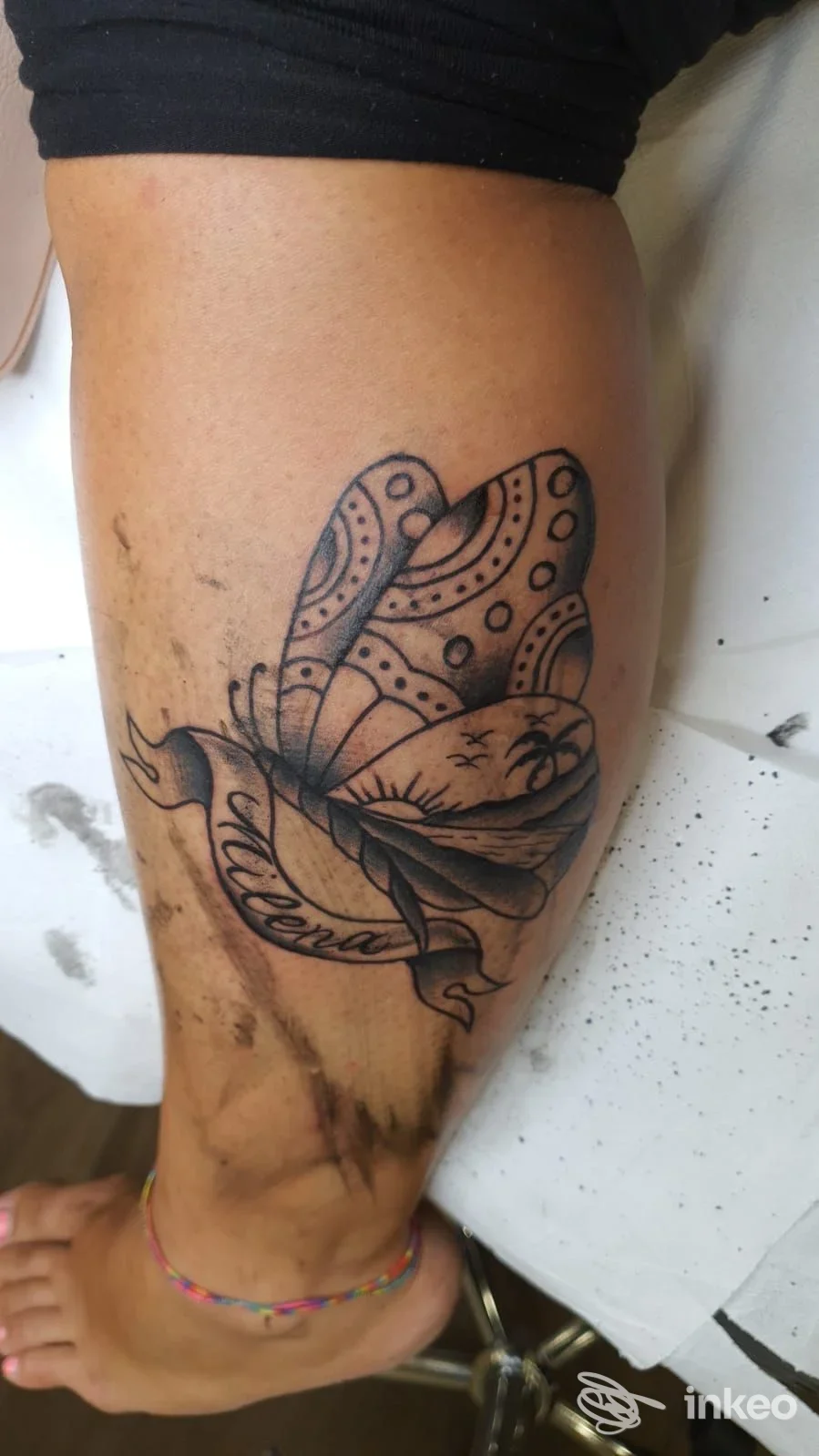Tatuaggio nero a forma di farfalla con paesaggio e nastro sul polpaccio, Dark Old Tattoo, Roma.