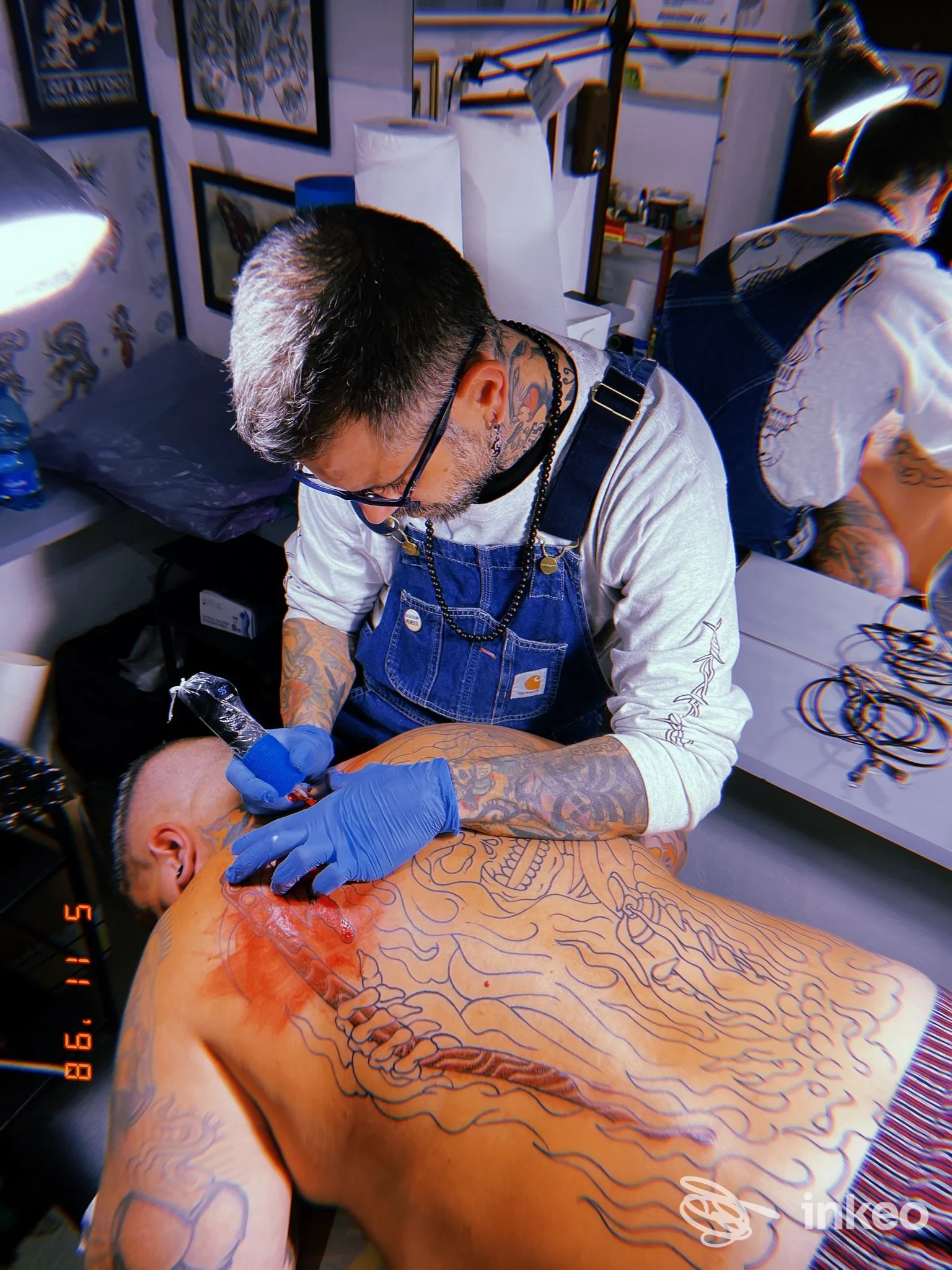Attività di tatuaggio sul dorso di una persona in uno studio: il tatuatore lavora sulle linee guida del tatuaggio sul dorso senza mostrare il volto completo.