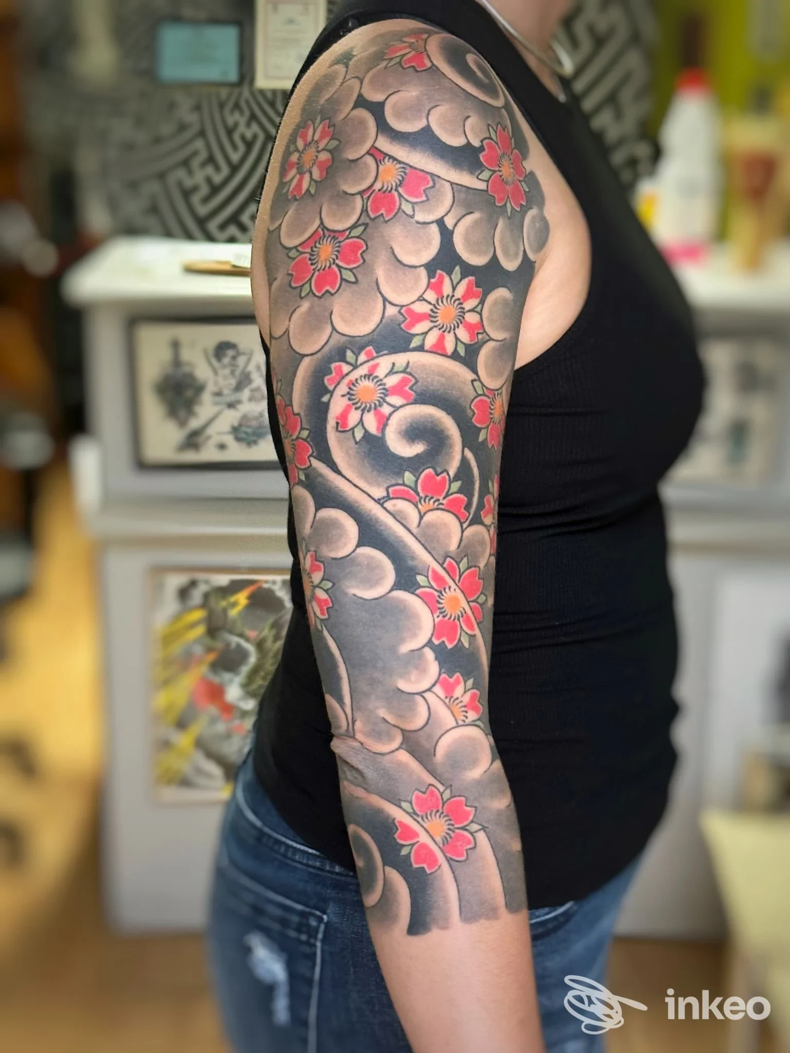 Manica tatuata sul braccio con nuvole scure e fiori rossi, scatto in studio Country life tattoo studio, Rieti.